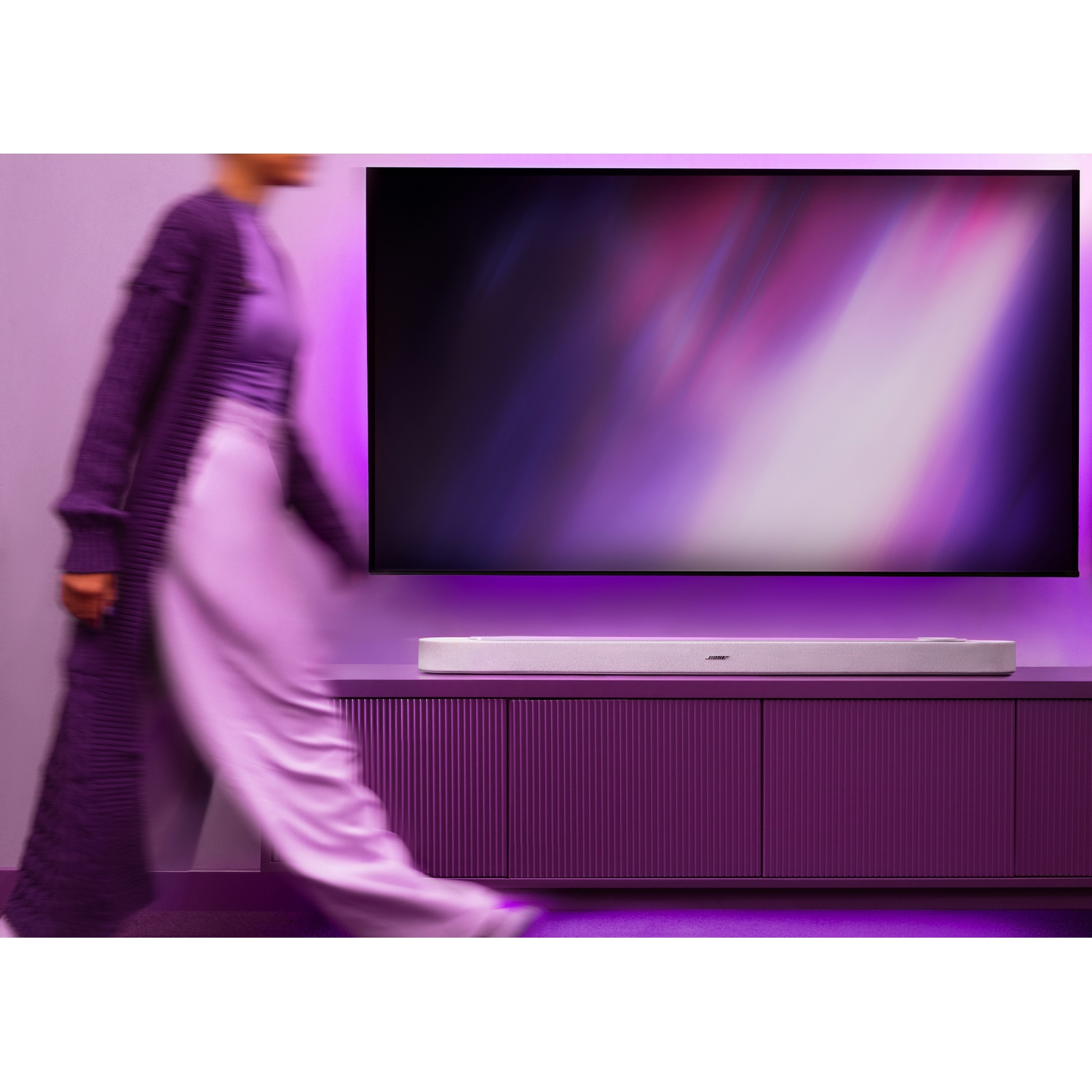 Una persona in viola passa davanti a una soundbar su un mobile viola sotto una TV.