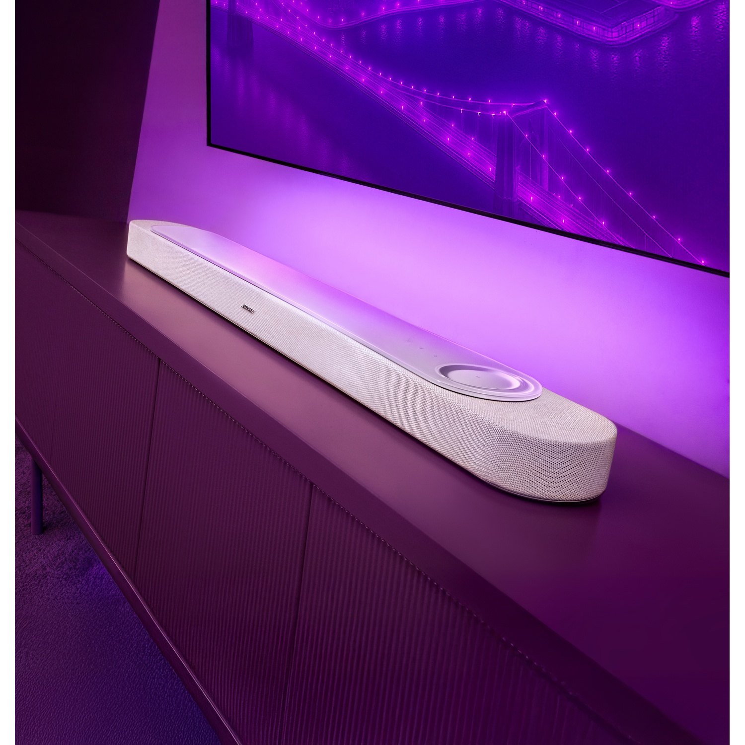 Un altoparlante bianco su un mobile viola sotto uno schermo illuminato di viola.