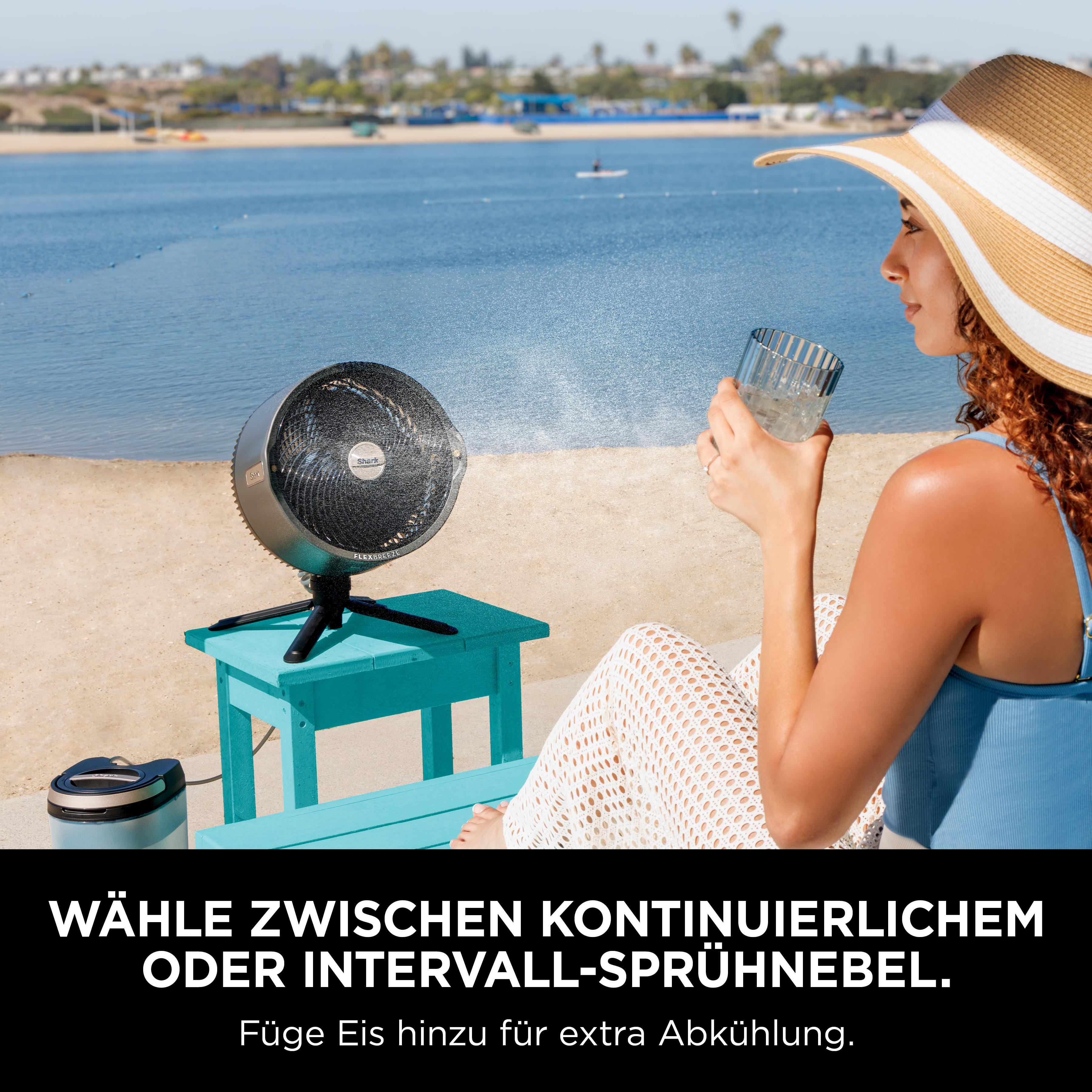 Frau mit Hut am Strand trinkt Glas, Ventilator auf Tisch.