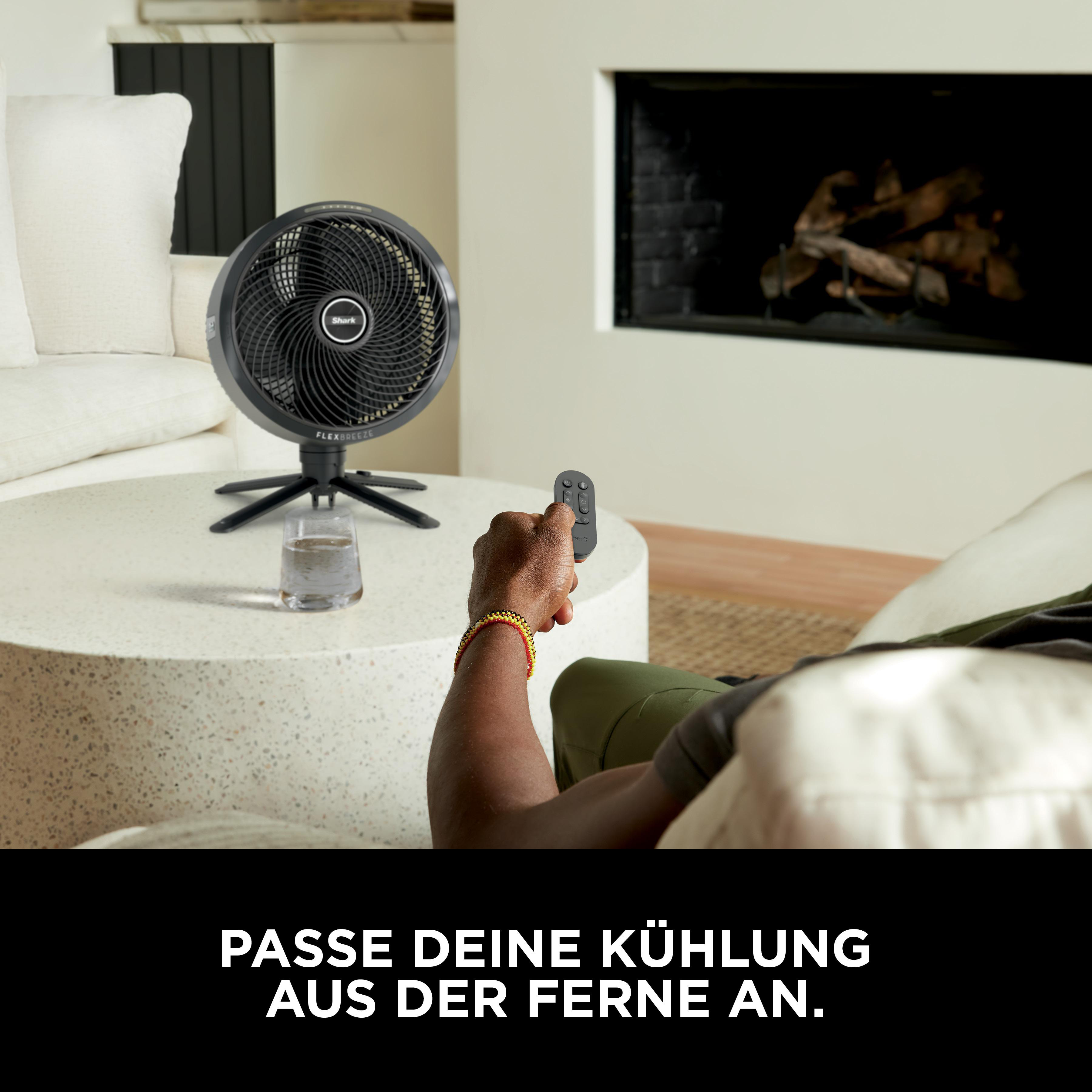 Ein Mann hält eine Fernbedienung und bedient einen Ventilator auf einem Tisch.