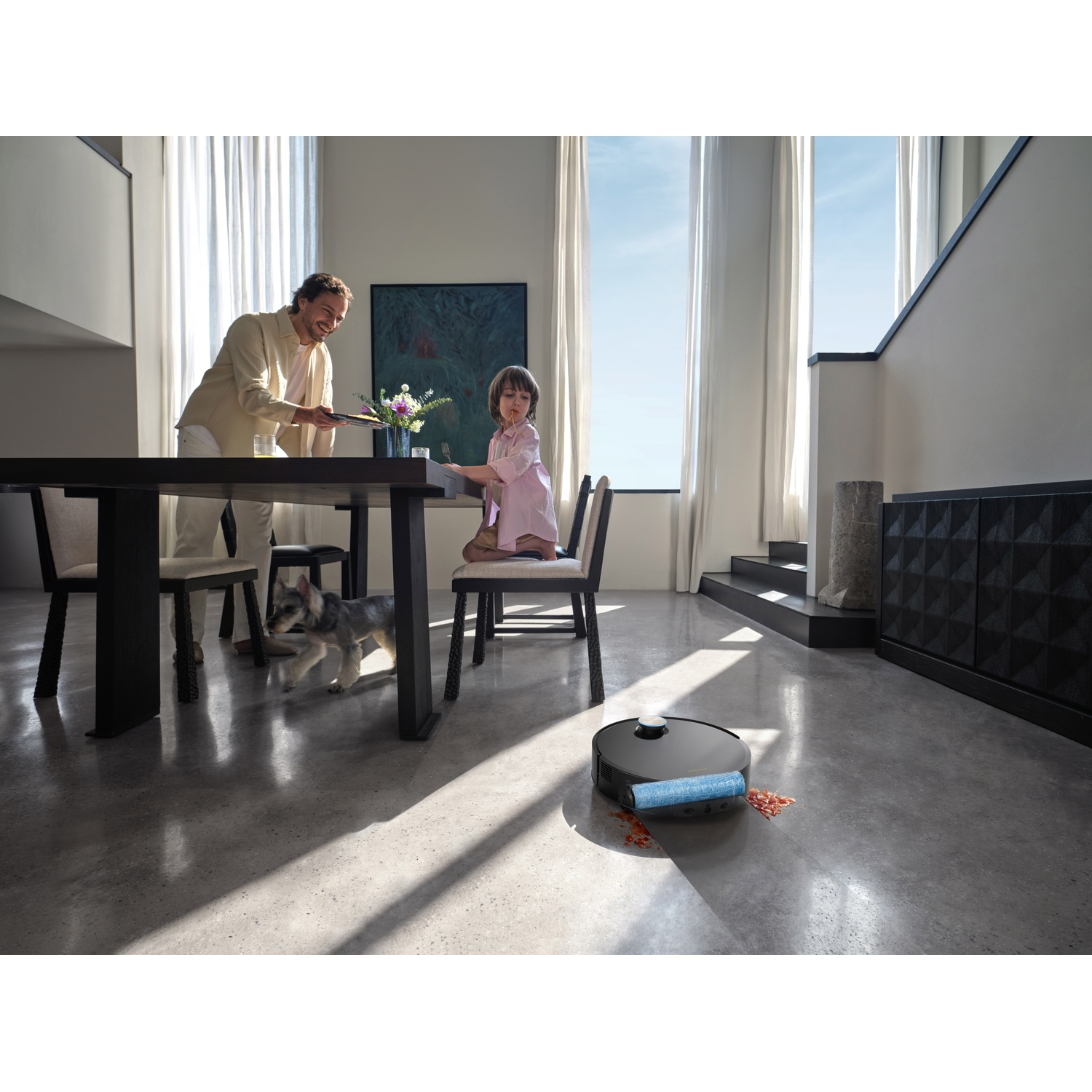 A robot vacuum cleans spilled food as a family eats at a table.