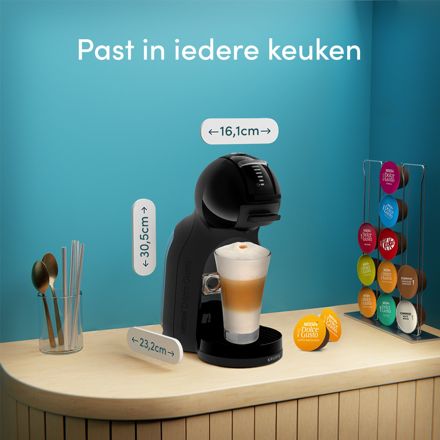Een zwarte Dolce Gusto koffiemachine met een latte macchiato, cups en lepels.