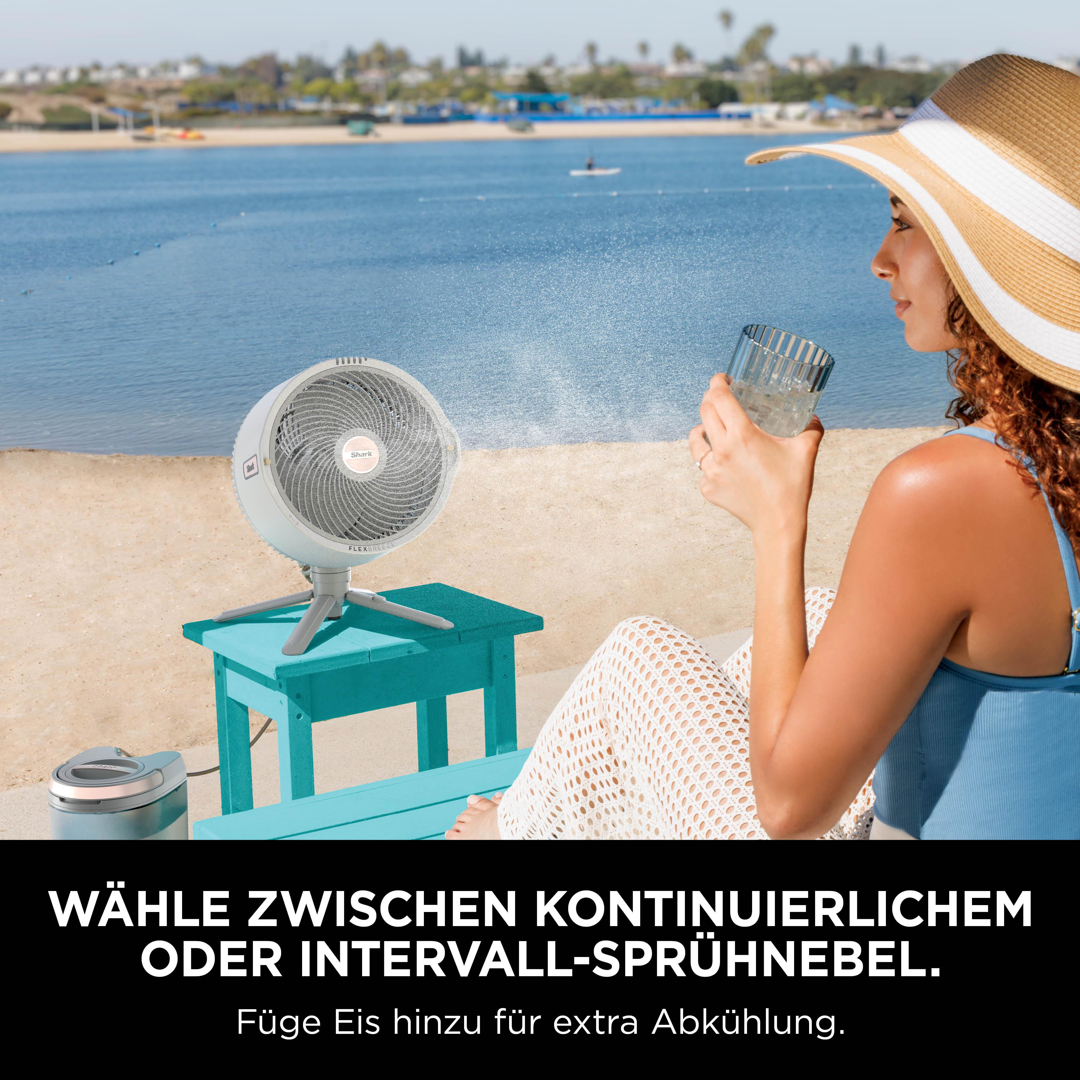 Eine Frau mit Hut trinkt ein Glas Wasser am Strand neben einem Ventilator.