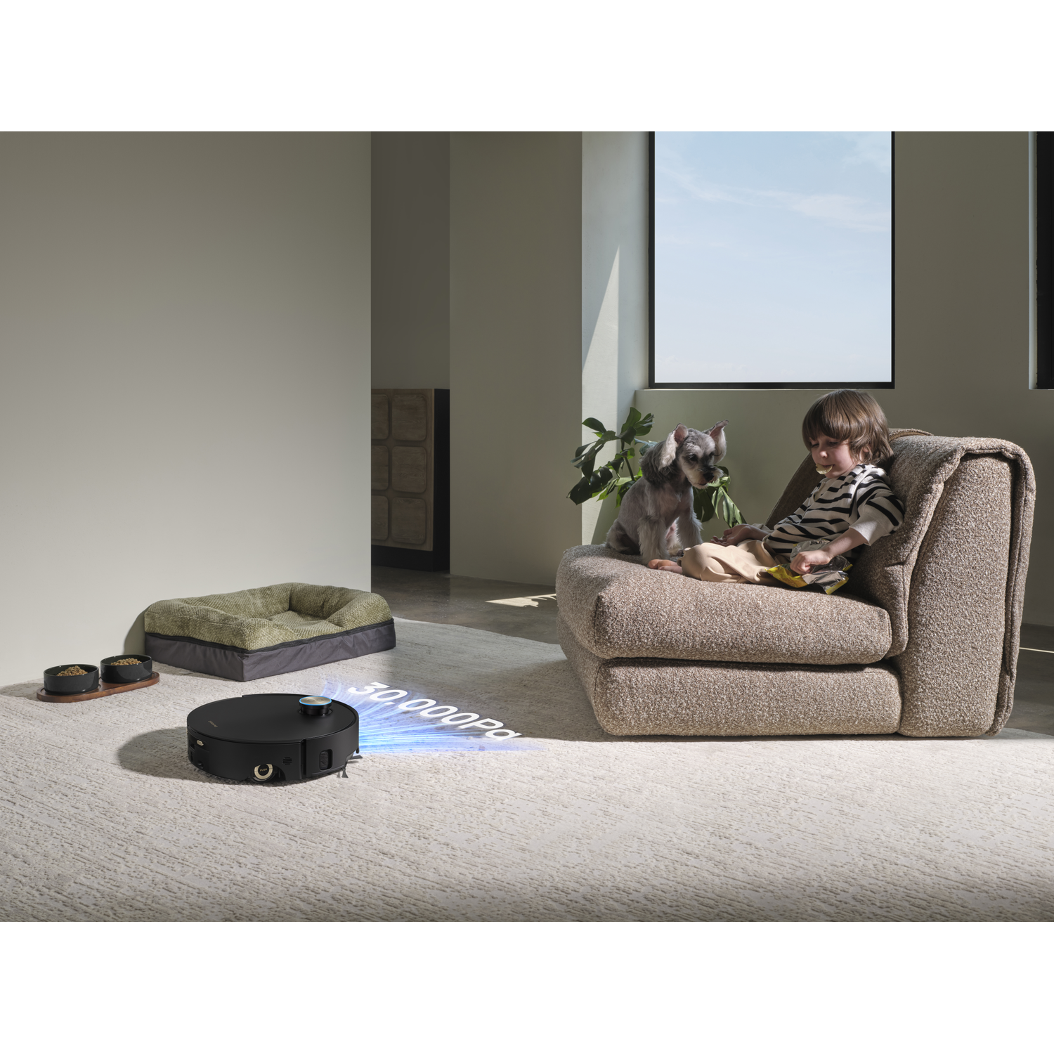 Een robotstofzuiger maakt een tapijt schoon terwijl een kind met een hond op een fauteuil zit.