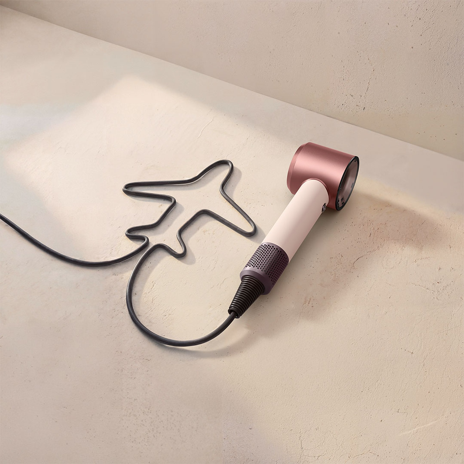 A hairdryer with its cord shaped like an airplane on a concrete floor.