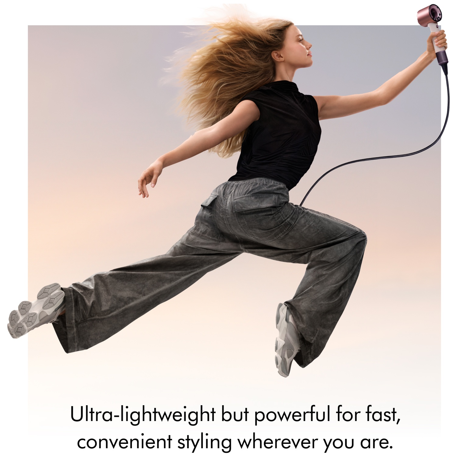 Woman jumping mid-air holding a hairdryer, blonde hair blowing in the wind.