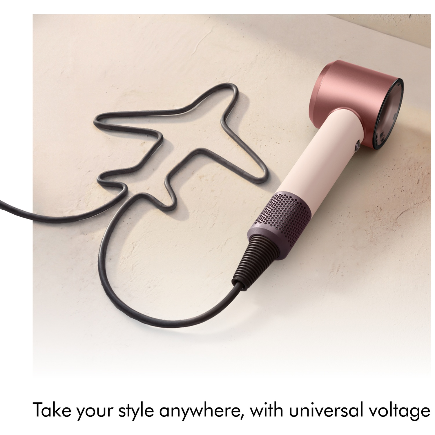 A rose gold hairdryer with a black cord shaped like an airplane on a light surface.
