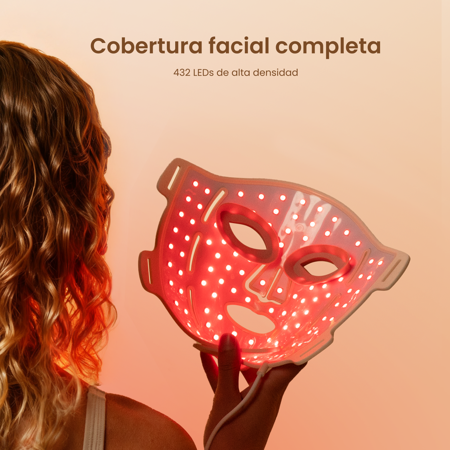 Una mujer sostiene una mascarilla facial LED roja sobre un fondo naranja cálido.