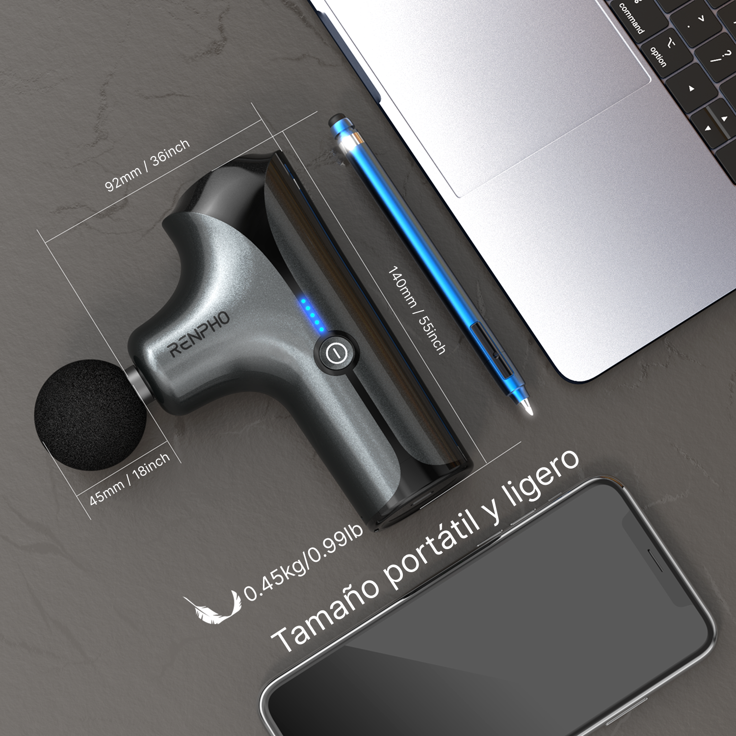 Pistola de masaje gris con cabezal negro junto a portátil y teléfono.