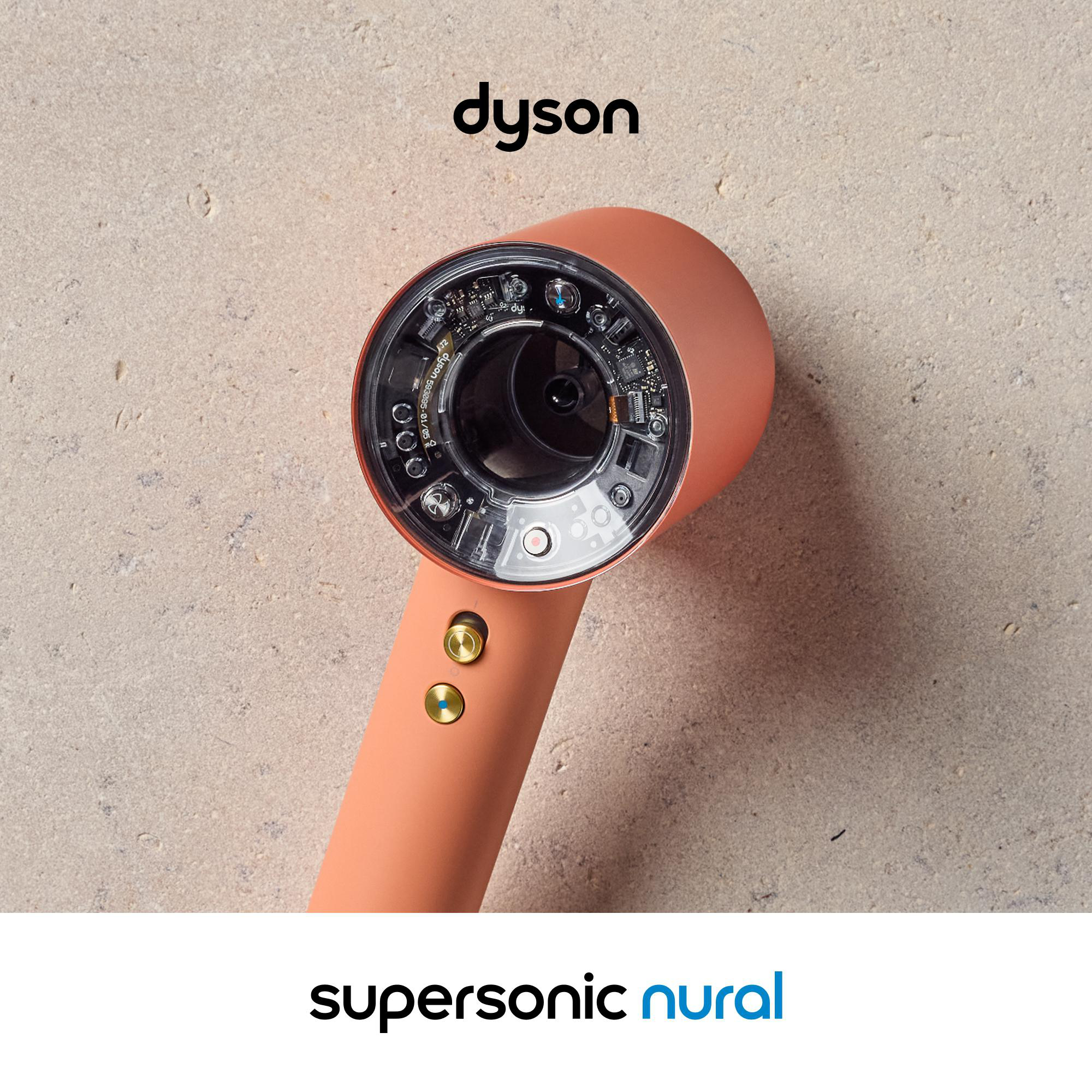 Ein korallenfarbener Dyson Supersonic Haartrockner mit sichtbarer Technik auf einer Steintextur.