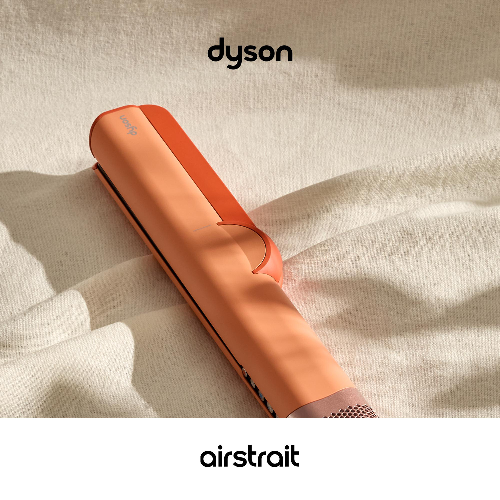 Ein korallenfarbener Dyson Airstrait Haarglätter liegt auf einem beigefarbenen Stoff.