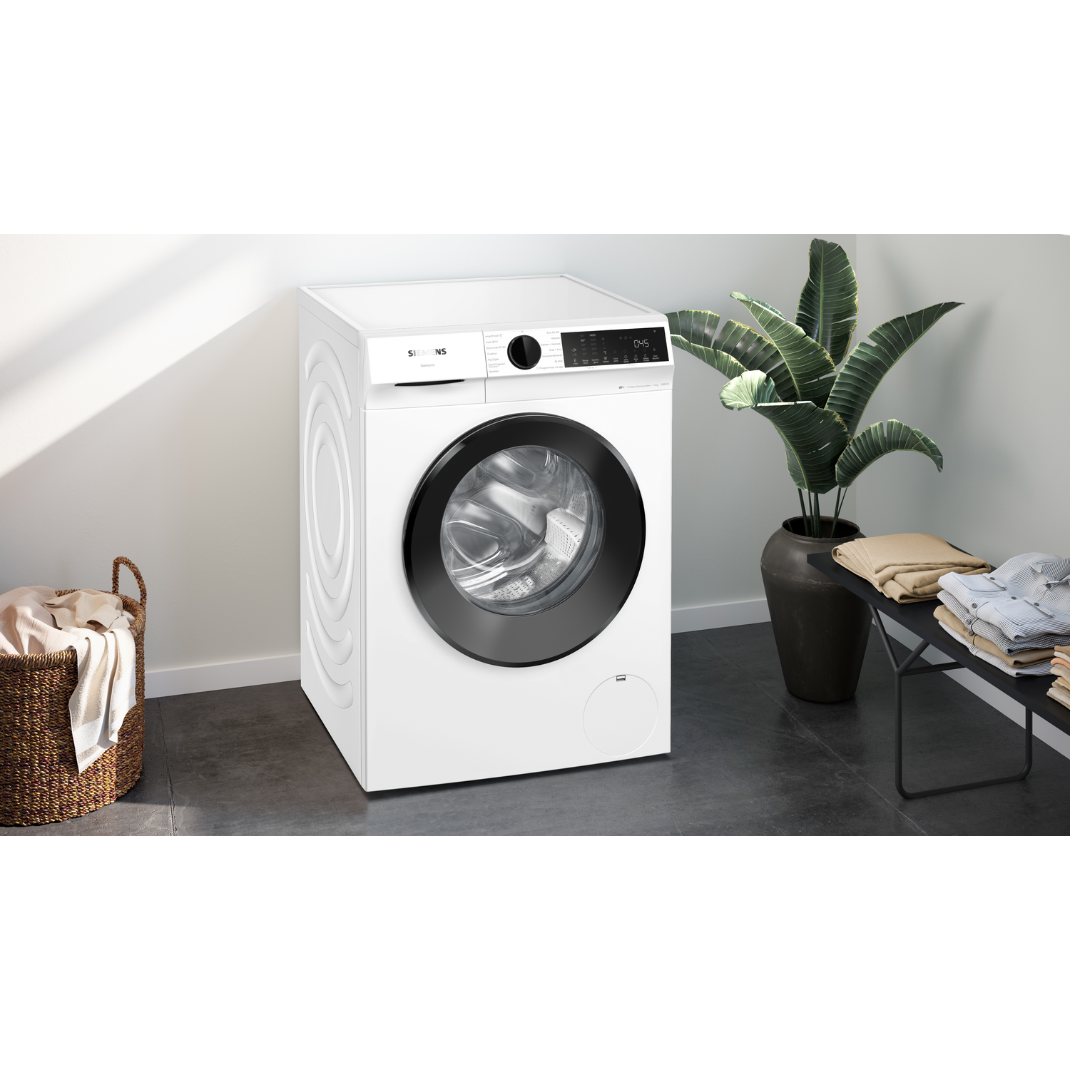 White washing machine with black door, laundry basket, and plants.