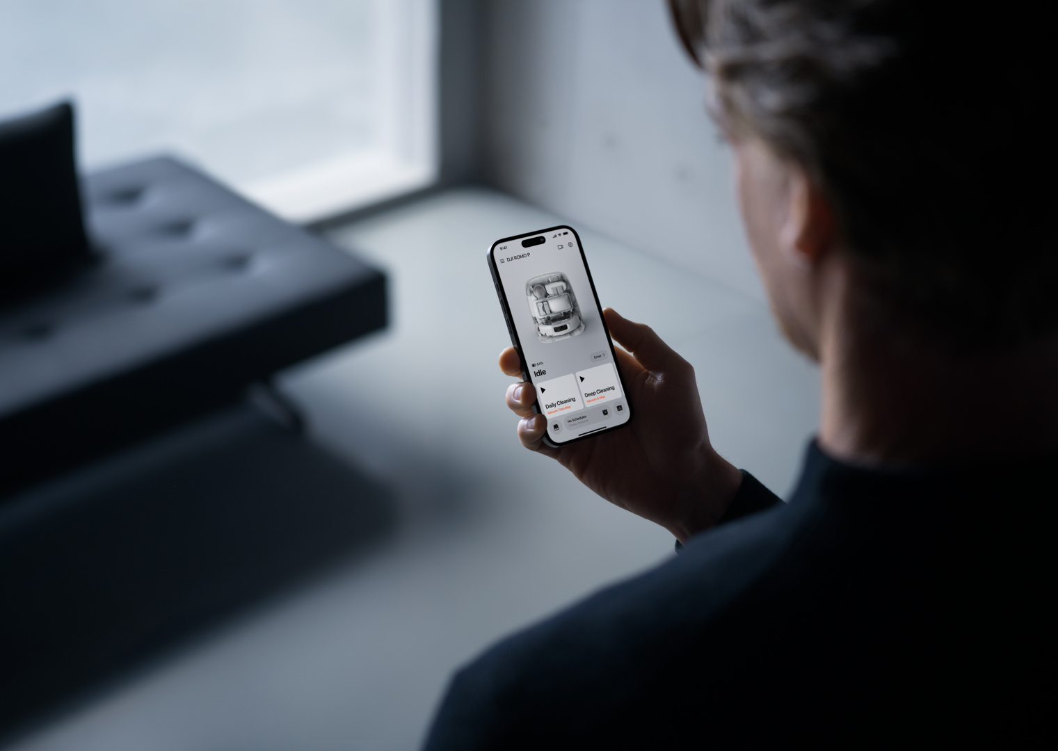 Uomo tiene smartphone con app pulizia robot. Display mostra modalità di pulizia.