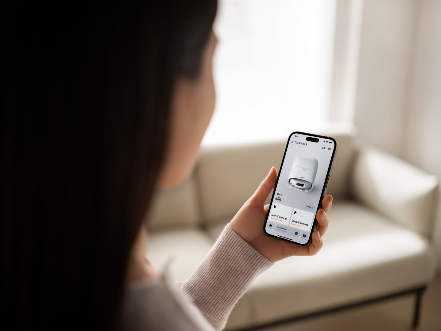 Una persona tiene uno smartphone che mostra un'app per robot aspirapolvere con immagine e opzioni.