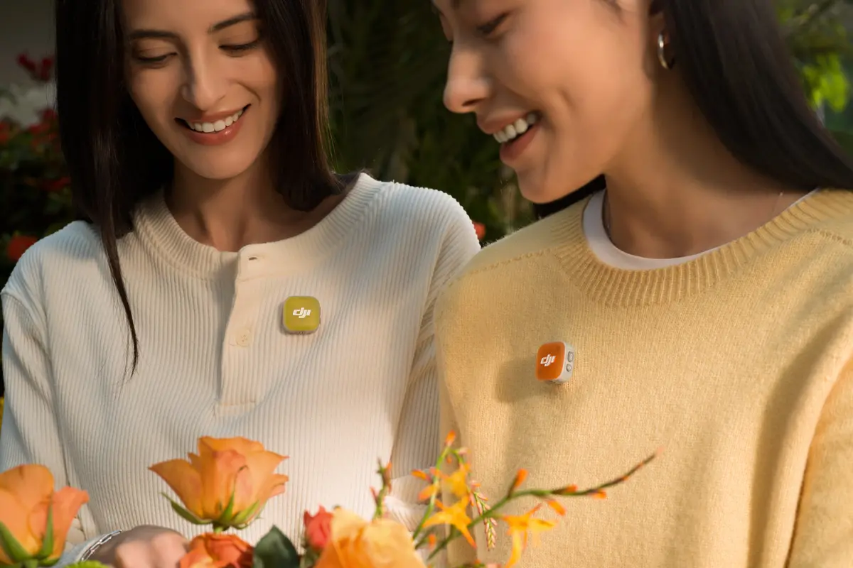 Deux femmes sourient, portent des badges colorés et tiennent des fleurs.