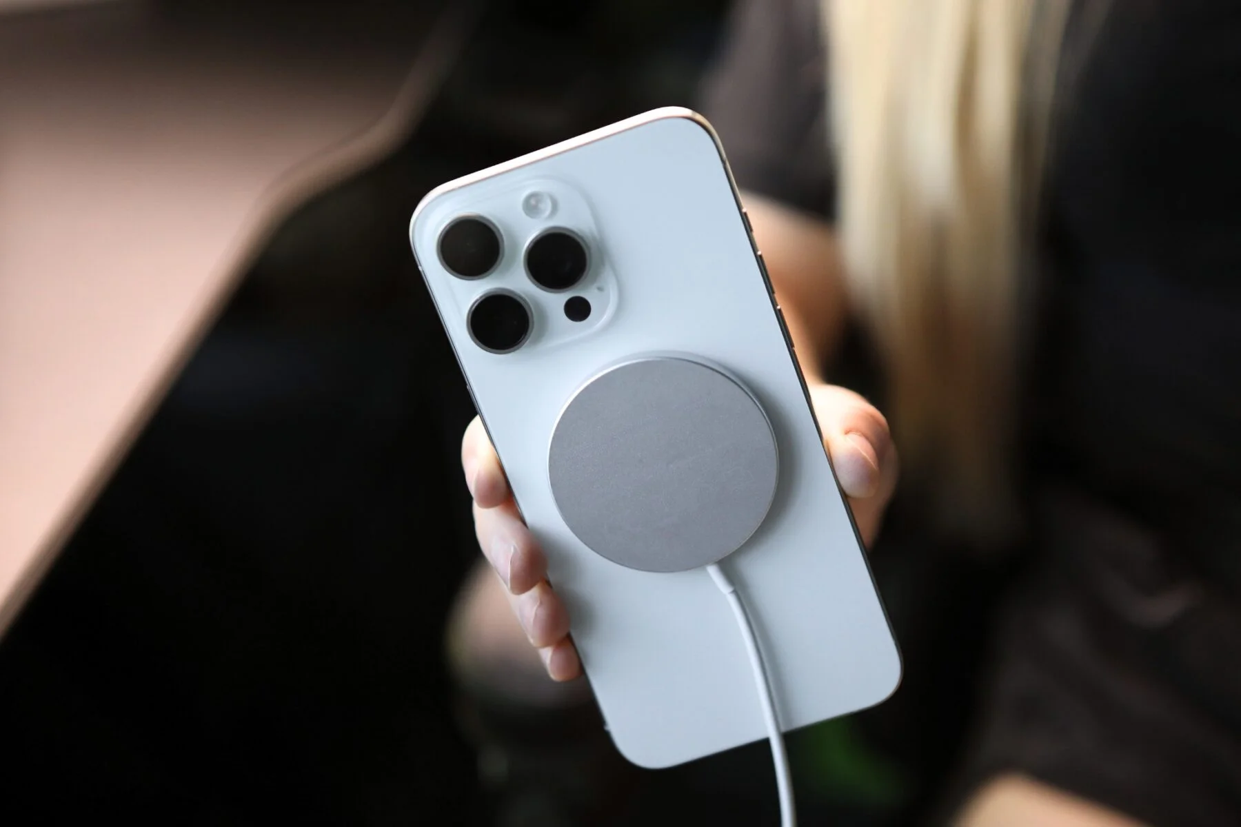 Egy fehér iPhone hátlap három kamerával és egy kerek mágneses töltővel.