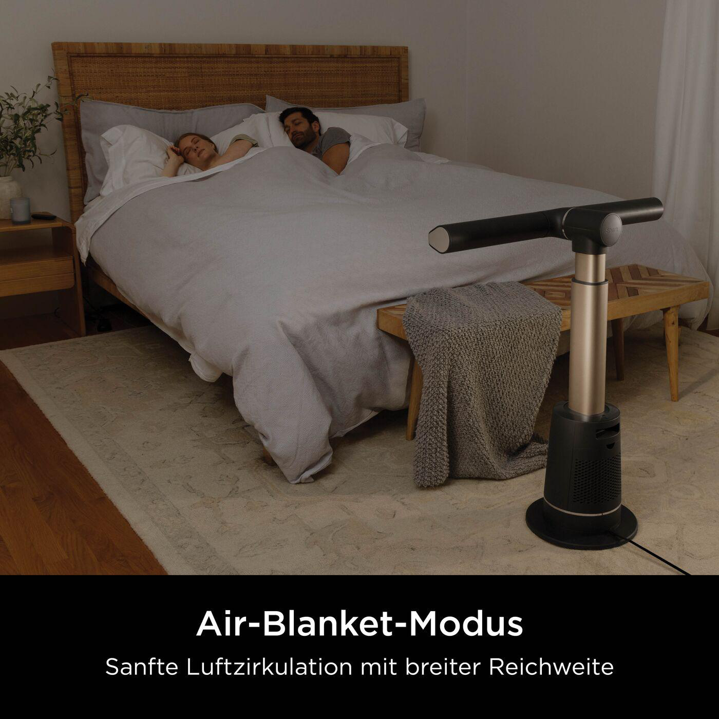 Ein Paar schläft unter einer Decke in einem Bett, ein Ventilator steht daneben.