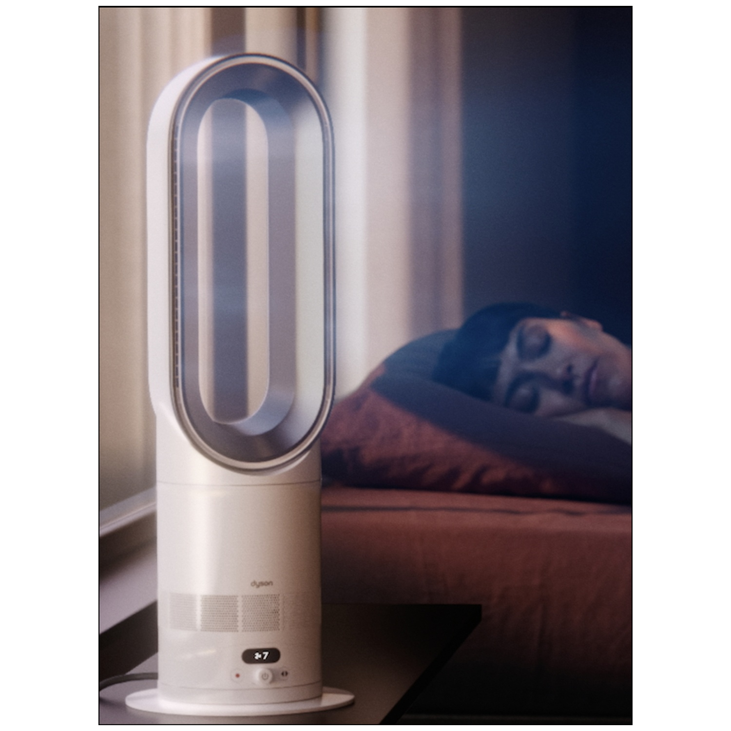 Een witte Dyson ventilator naast een slapende man op een bed.