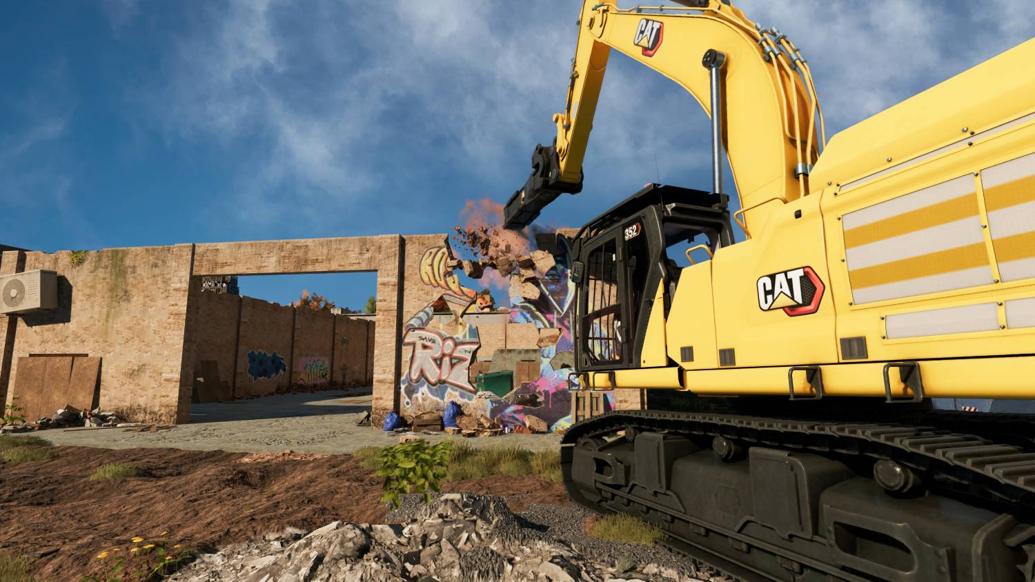 Una excavadora amarilla demuele una pared con grafitis, volando polvo y escombros.
