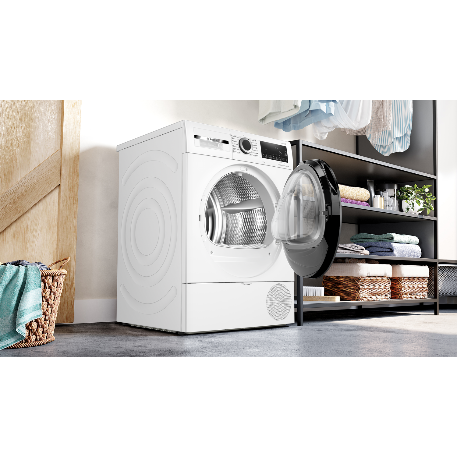A white dryer with an open door sits next to a laundry basket. Shelves with laundry are behind it.