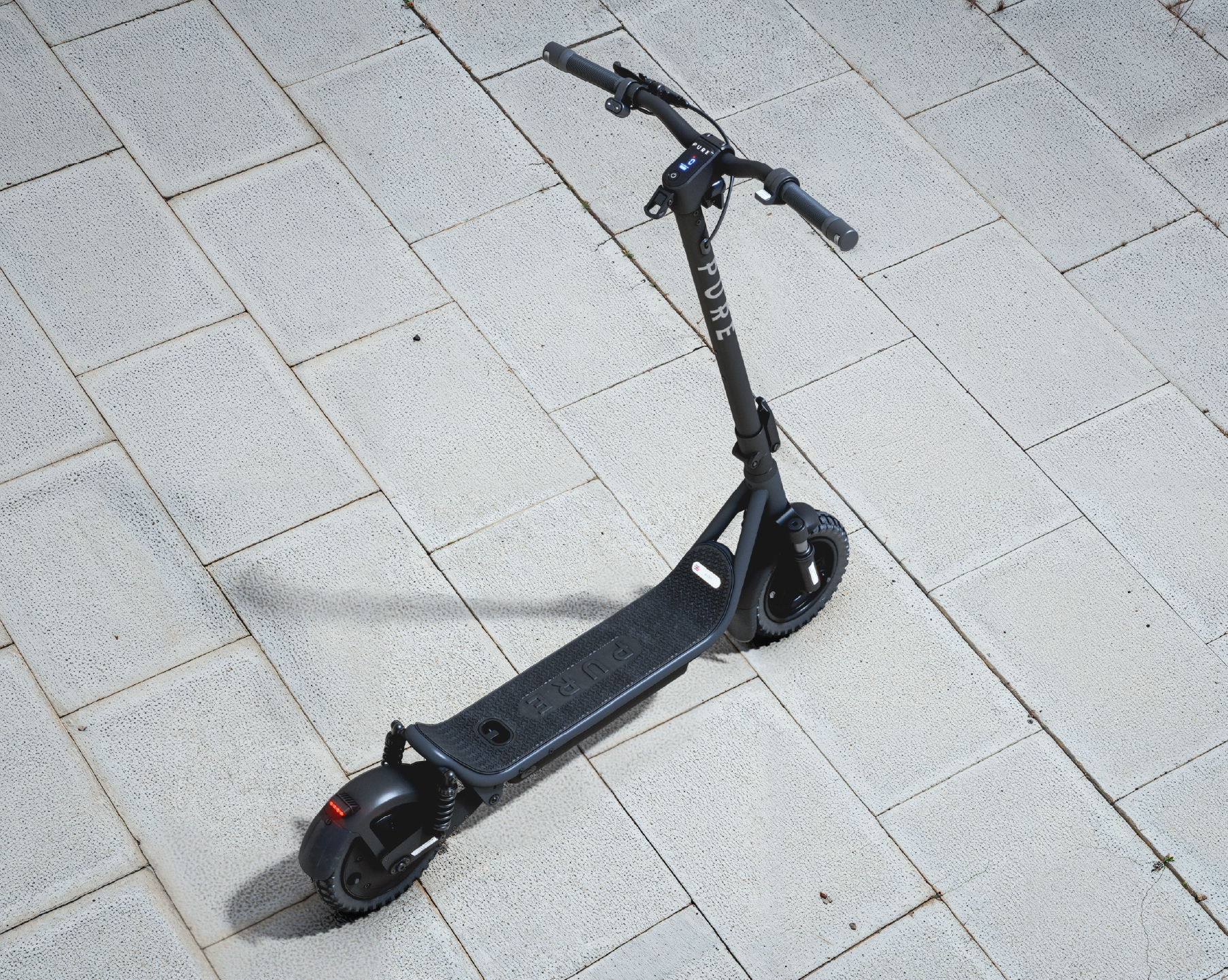 Ein schwarzer Elektroroller steht auf einem Gehweg aus hellgrauen Platten.