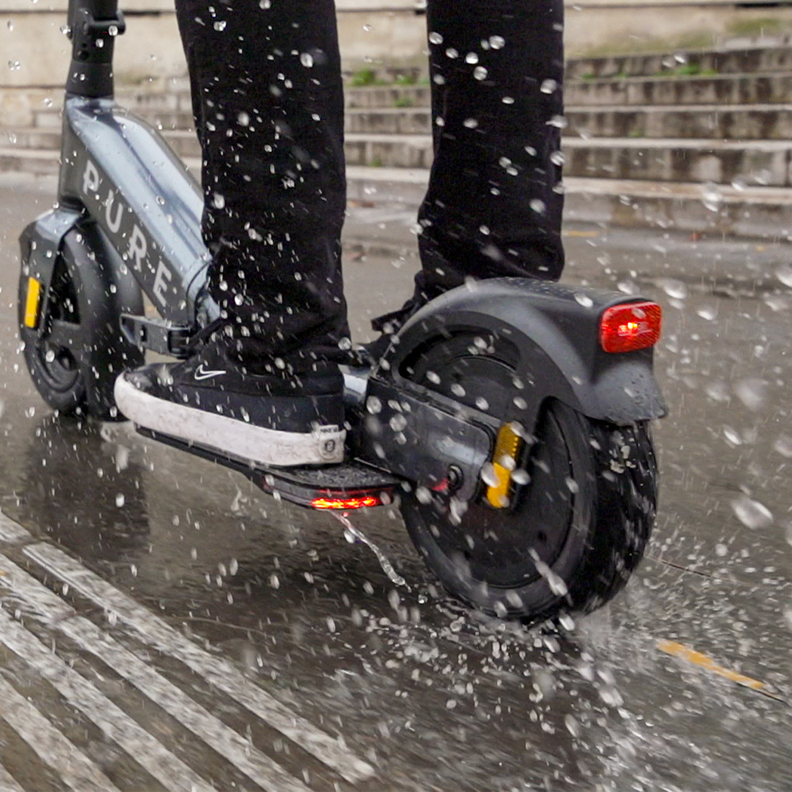 Person fährt Elektroroller durch Wasserpfützen auf Asphalt.