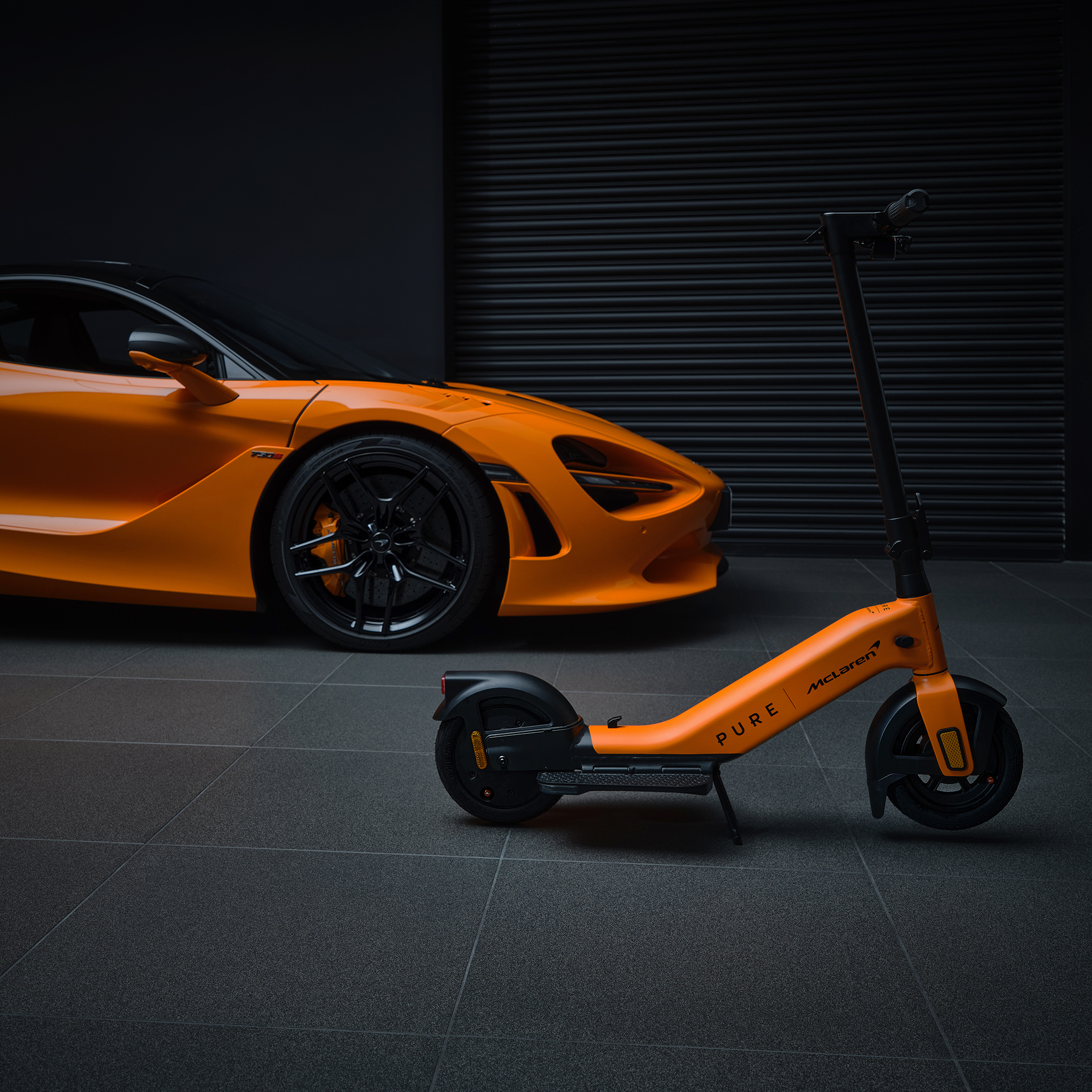 Ein orangefarbener McLaren und ein orangefarbener E-Scooter stehen nebeneinander.