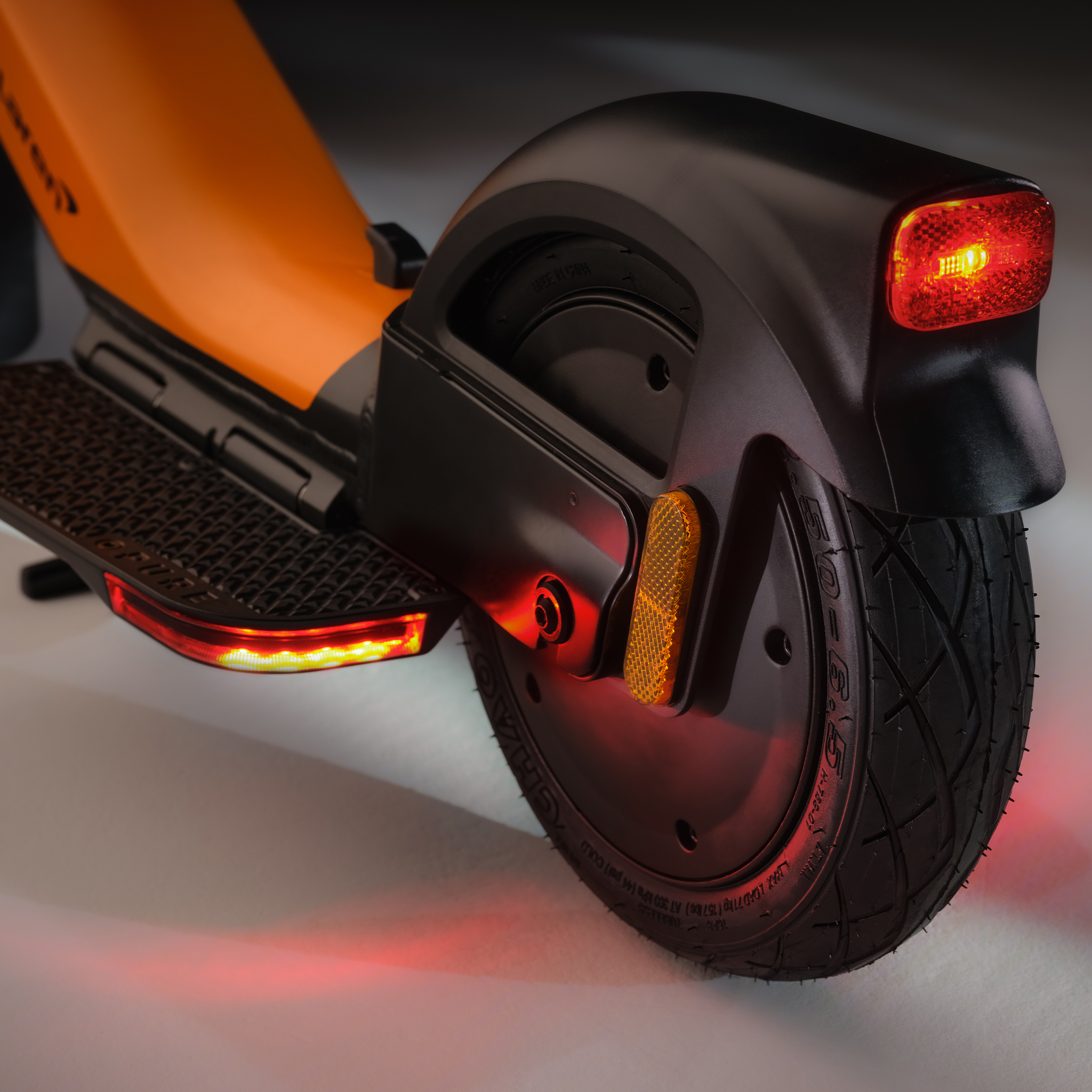 Nahaufnahme eines orangefarbenen Elektrorollers mit beleuchteten Rücklichtern.