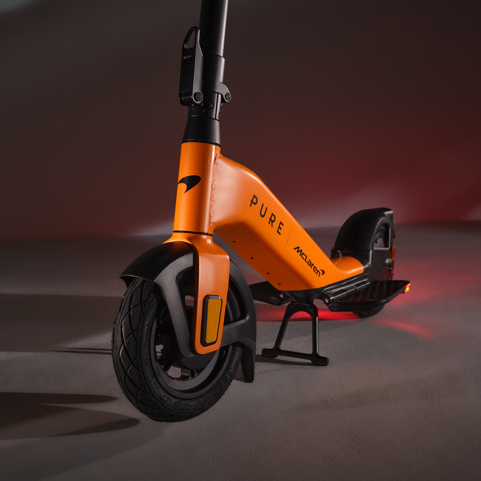 Ein orangefarbener Elektroroller mit schwarzen Akzenten steht auf einem Ständer.