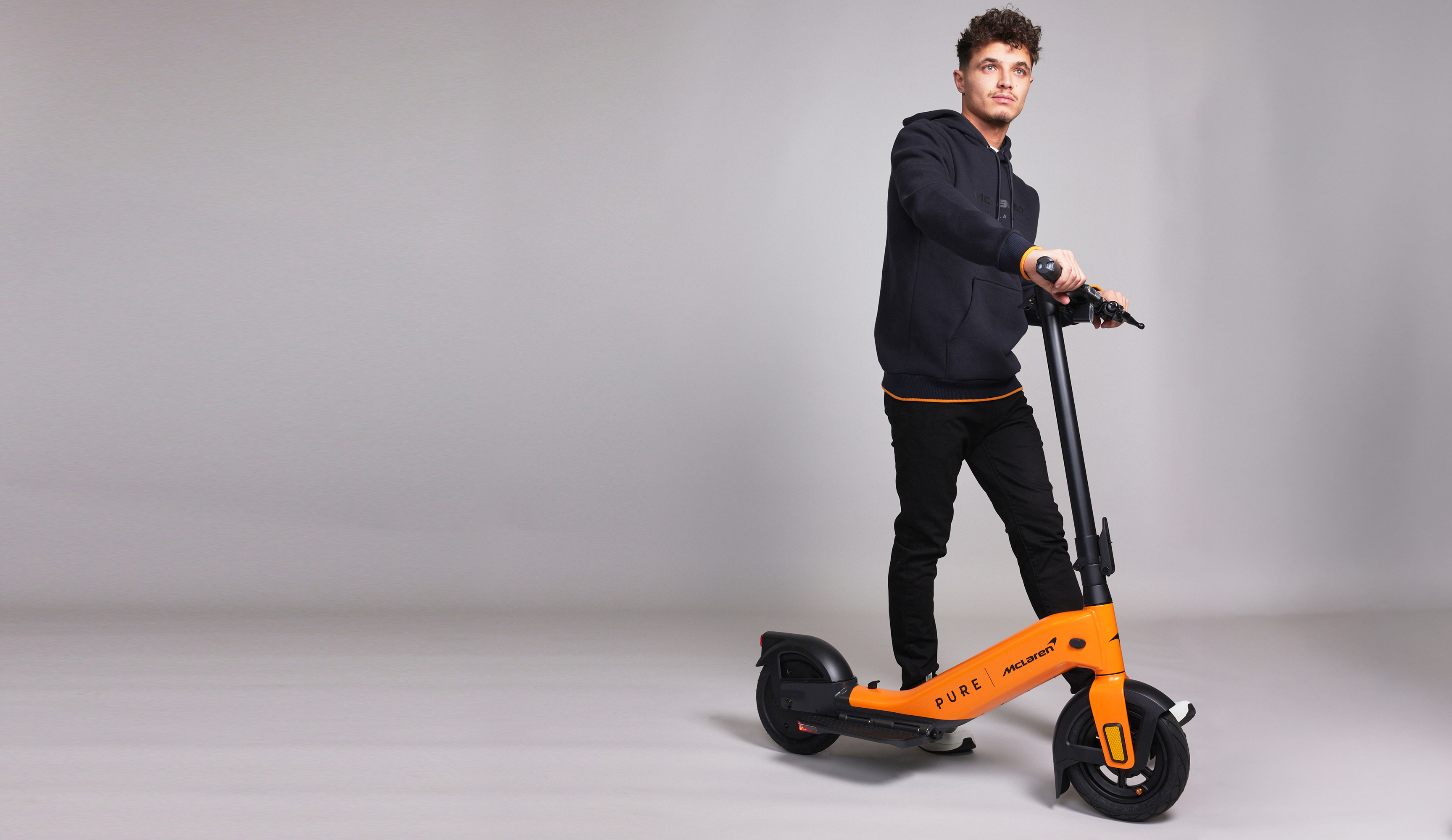 Mann mit dunklem Hoodie und Hose steht auf orangem E-Scooter.