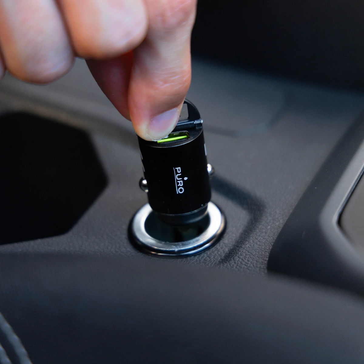 Eine Hand steckt einen schwarzen Puro-USB-Adapter in eine Auto-Buchse.