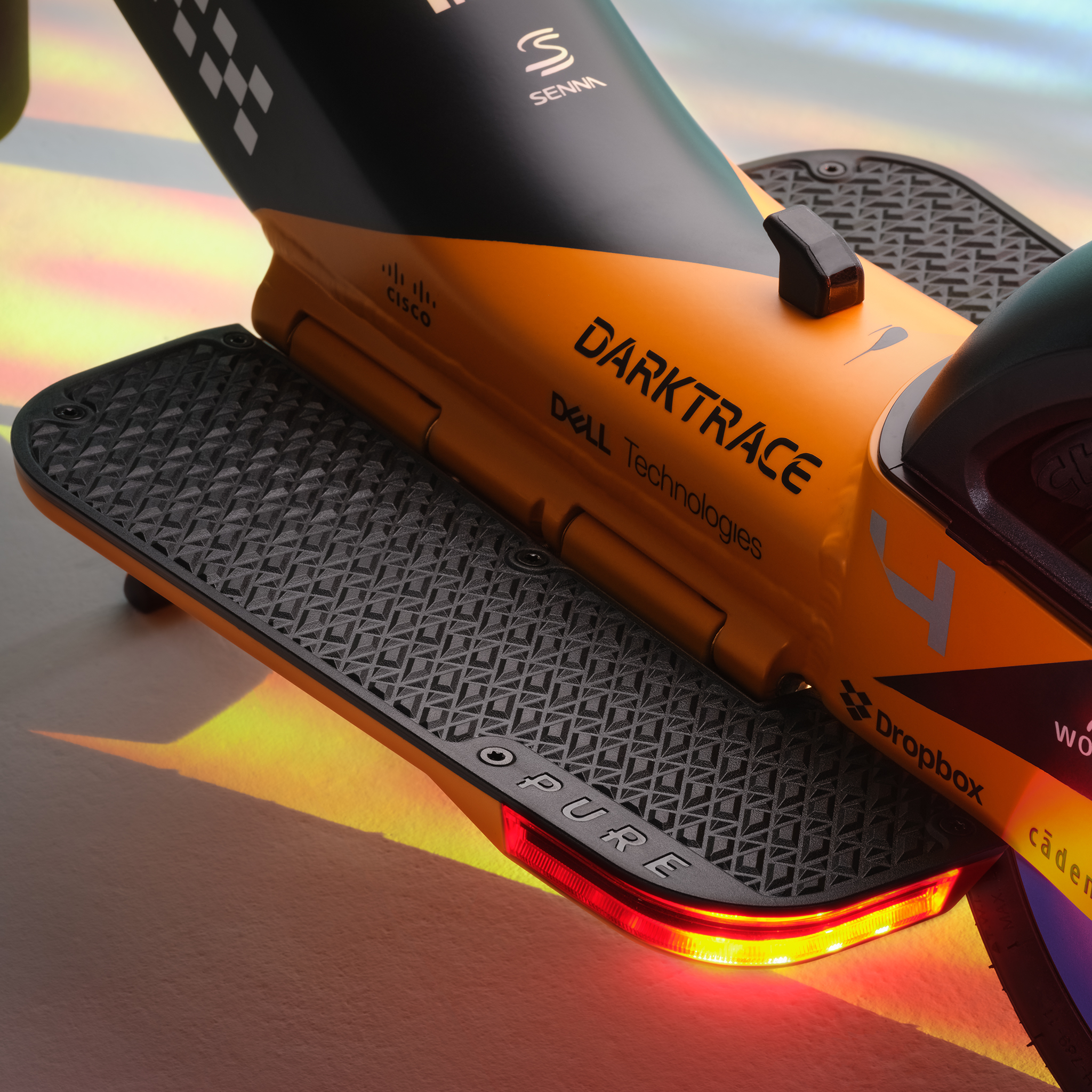 Orange-schwarzer Elektroroller mit „Darktrace“- und „Senna“-Logos. Strukturierte Trittflächen.
