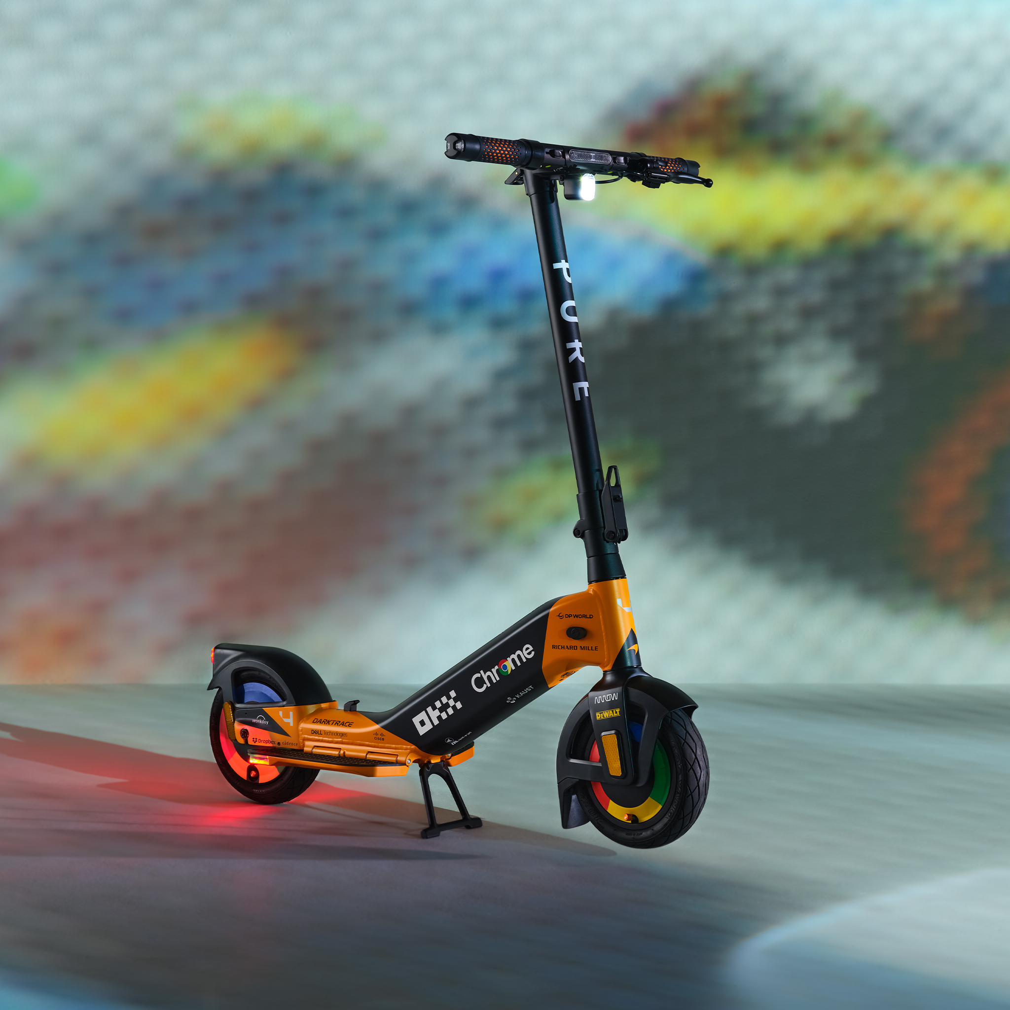 Ein orange-schwarzer Elektroroller mit Lichtern und Logos steht auf dem Boden.
