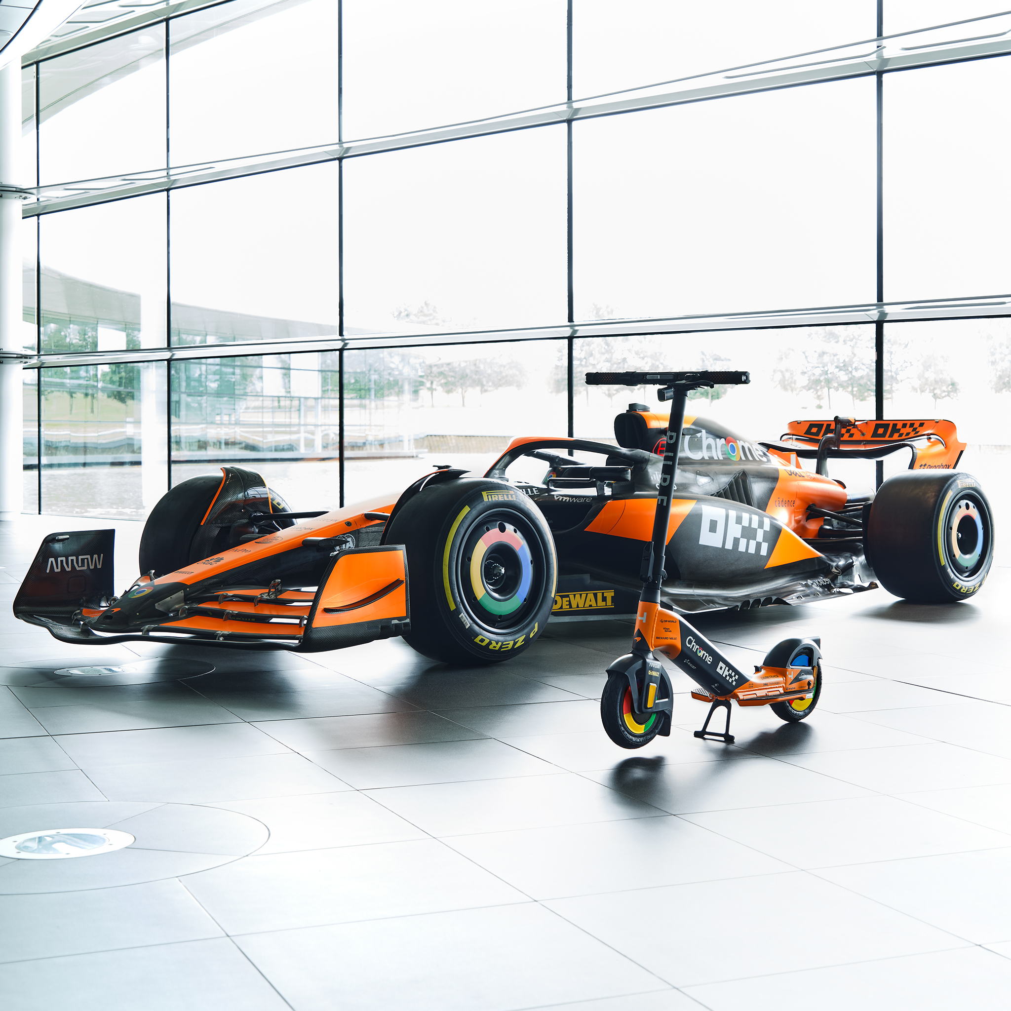 Ein Formel-1-Auto und ein E-Scooter stehen nebeneinander in einem hellen Raum.
