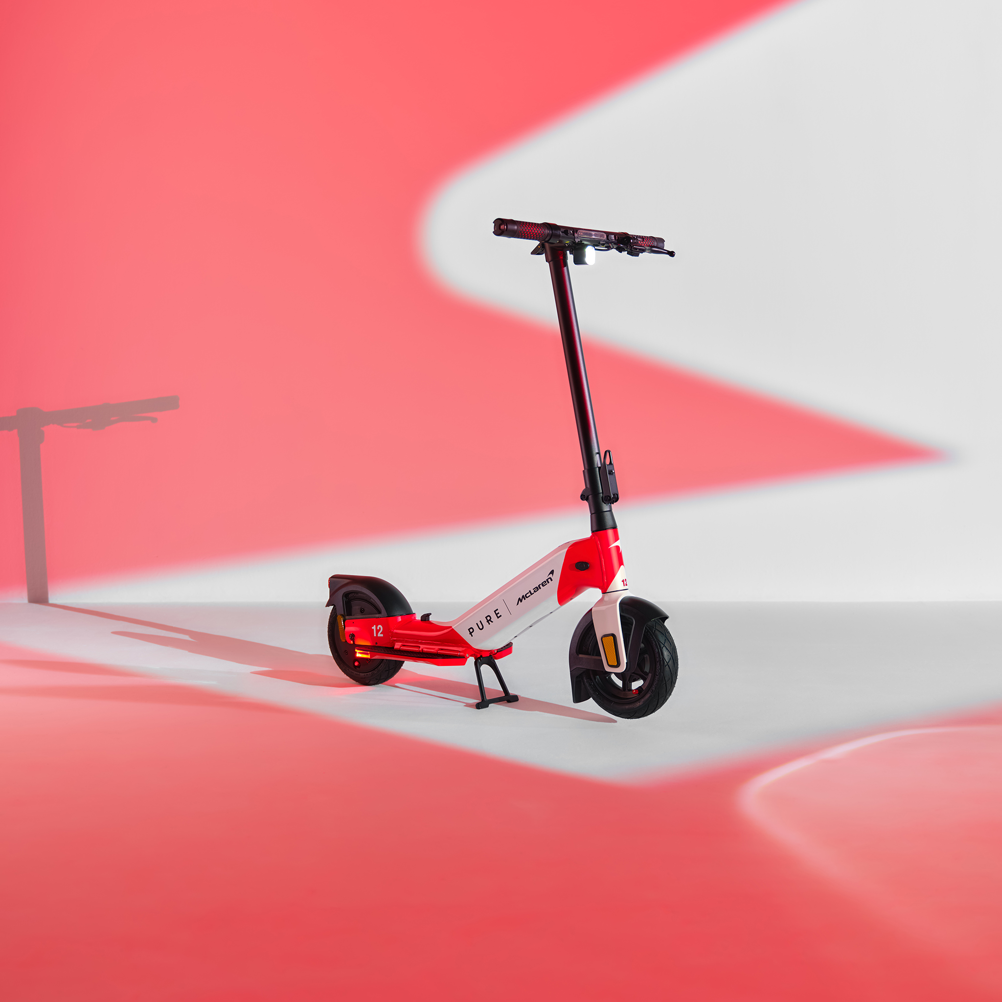 Ein roter und weißer E-Scooter mit schwarzem Lenker steht auf einem weißen Untergrund mit roten Lichtreflexionen.