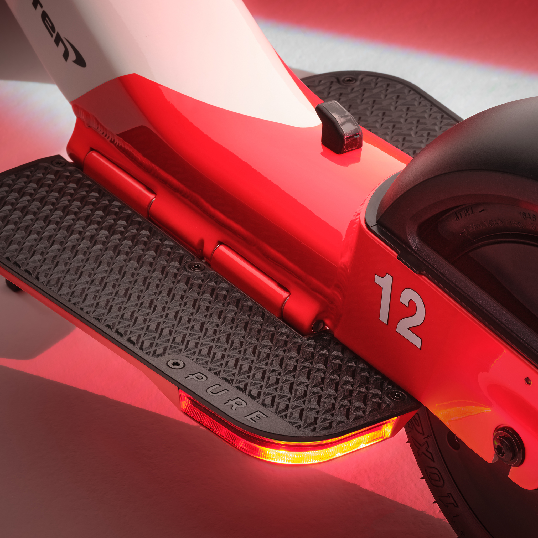 Detail eines rot-weißen Elektrorollers mit der Zahl 12 und beleuchtetem Rücklicht.