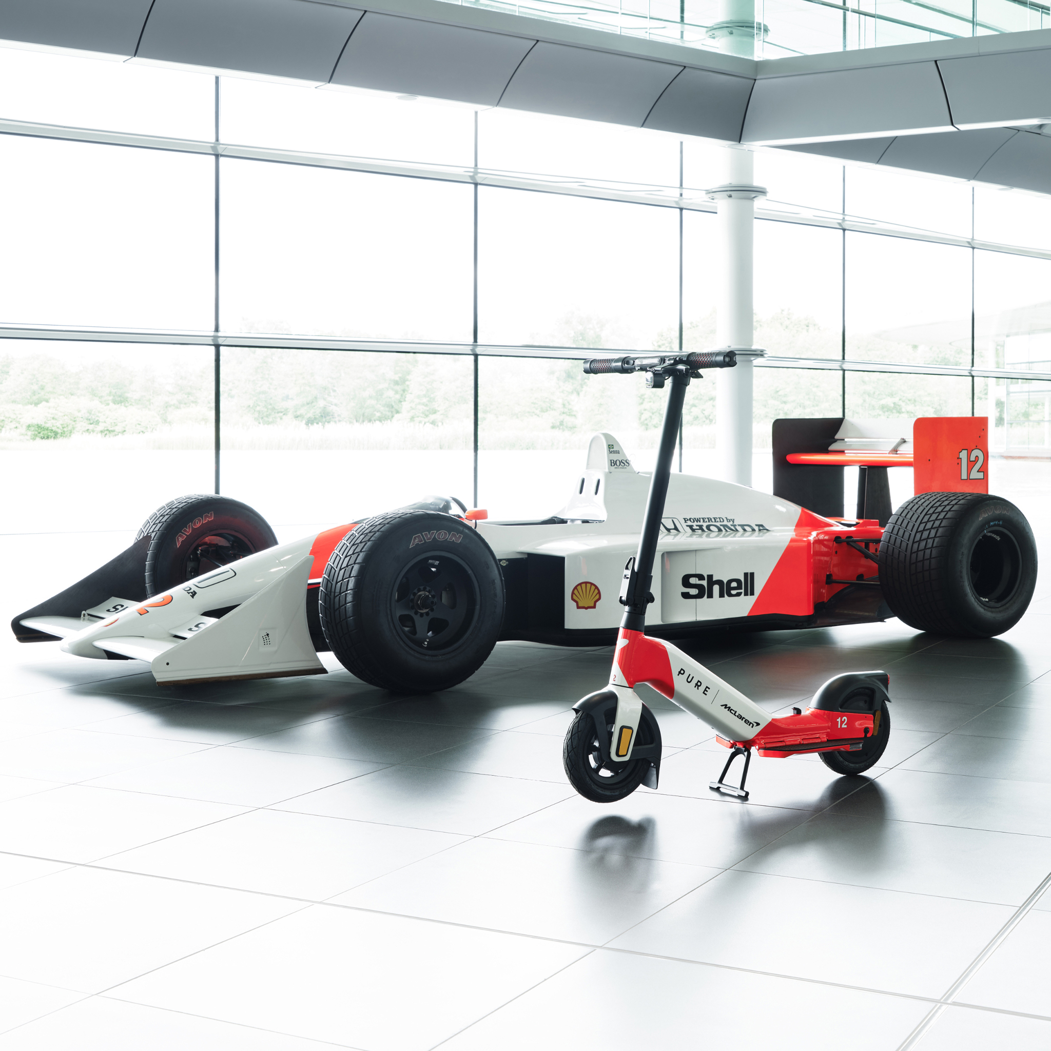 Ein Formel-1-Auto und ein E-Scooter stehen nebeneinander in einem hellen Raum.