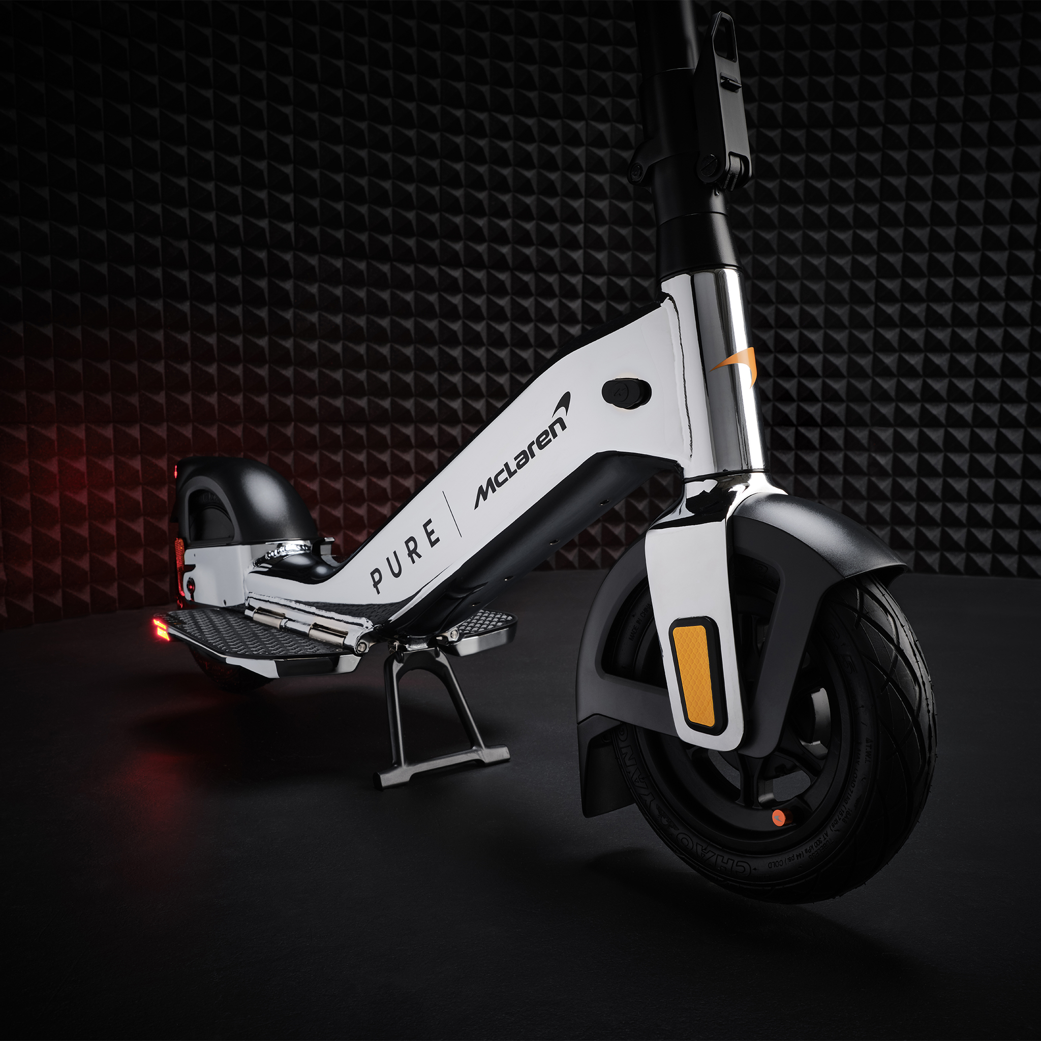 Ein weißer E-Scooter mit McLaren-Branding steht auf schwarzem Untergrund vor einer schwarzen Wand.