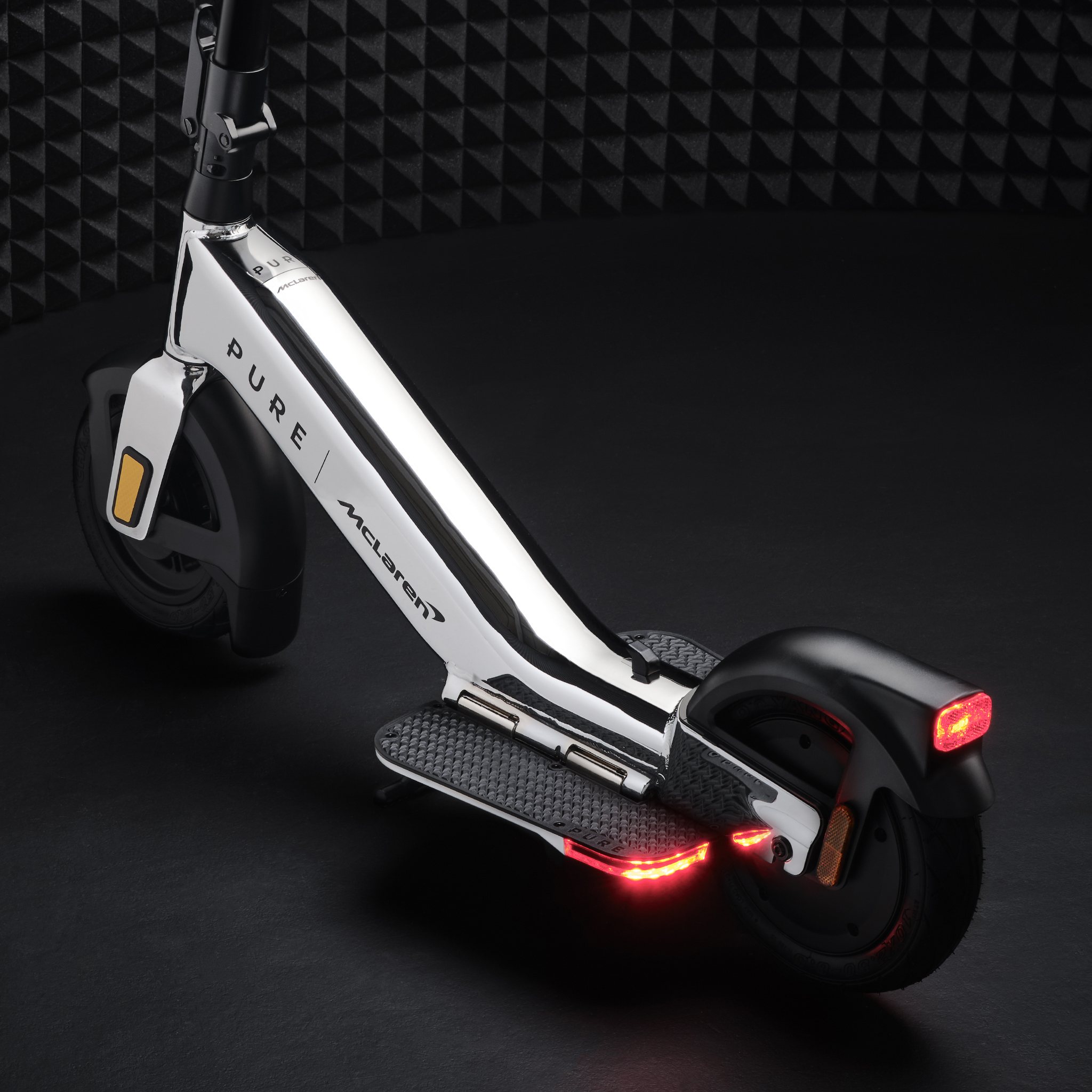 Ein weißer und verchromter Elektroroller mit roten Bremslichtern und 'Pure McLaren'-Branding.