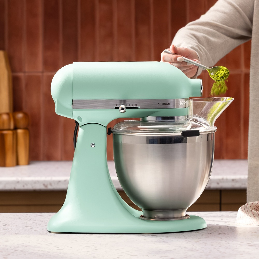 Una batidora de pie verde menta con bol de acero inoxidable se usa para agregar polvo verde.