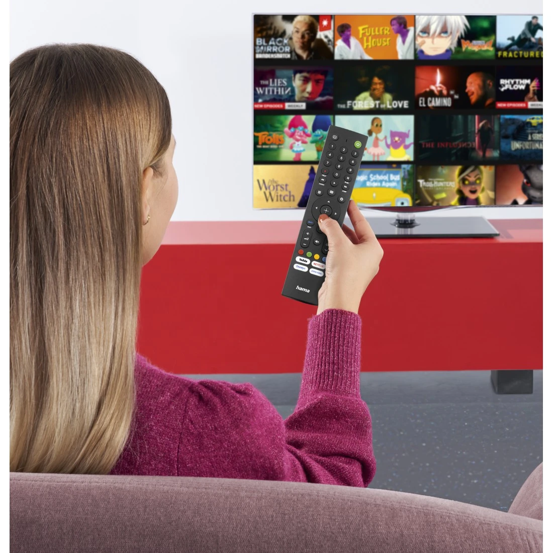 Una mujer sostiene un mando y mira una pantalla de TV con pósteres de películas.