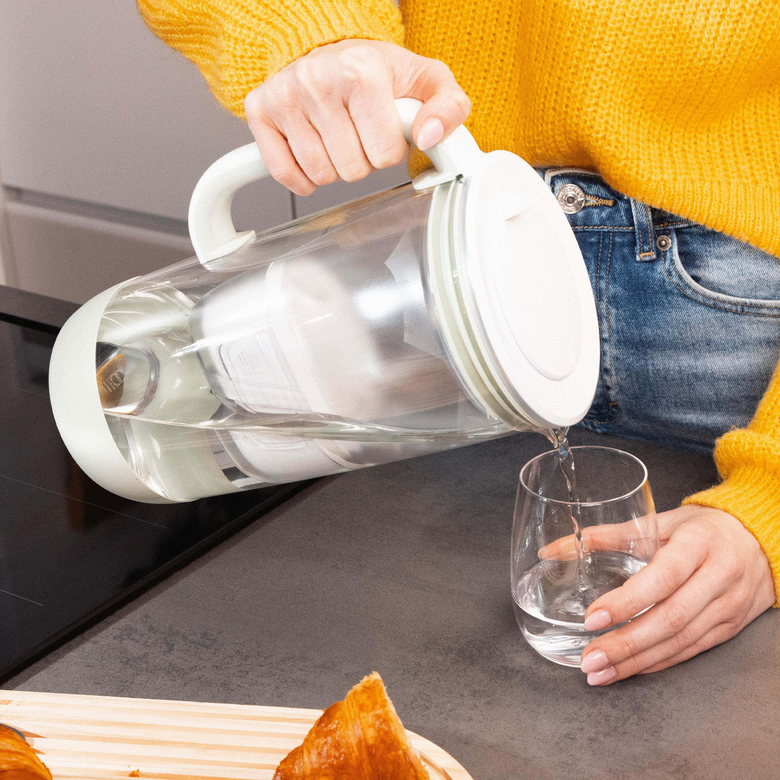 Eine Person gießt Wasser aus einer Karaffe in ein Glas.