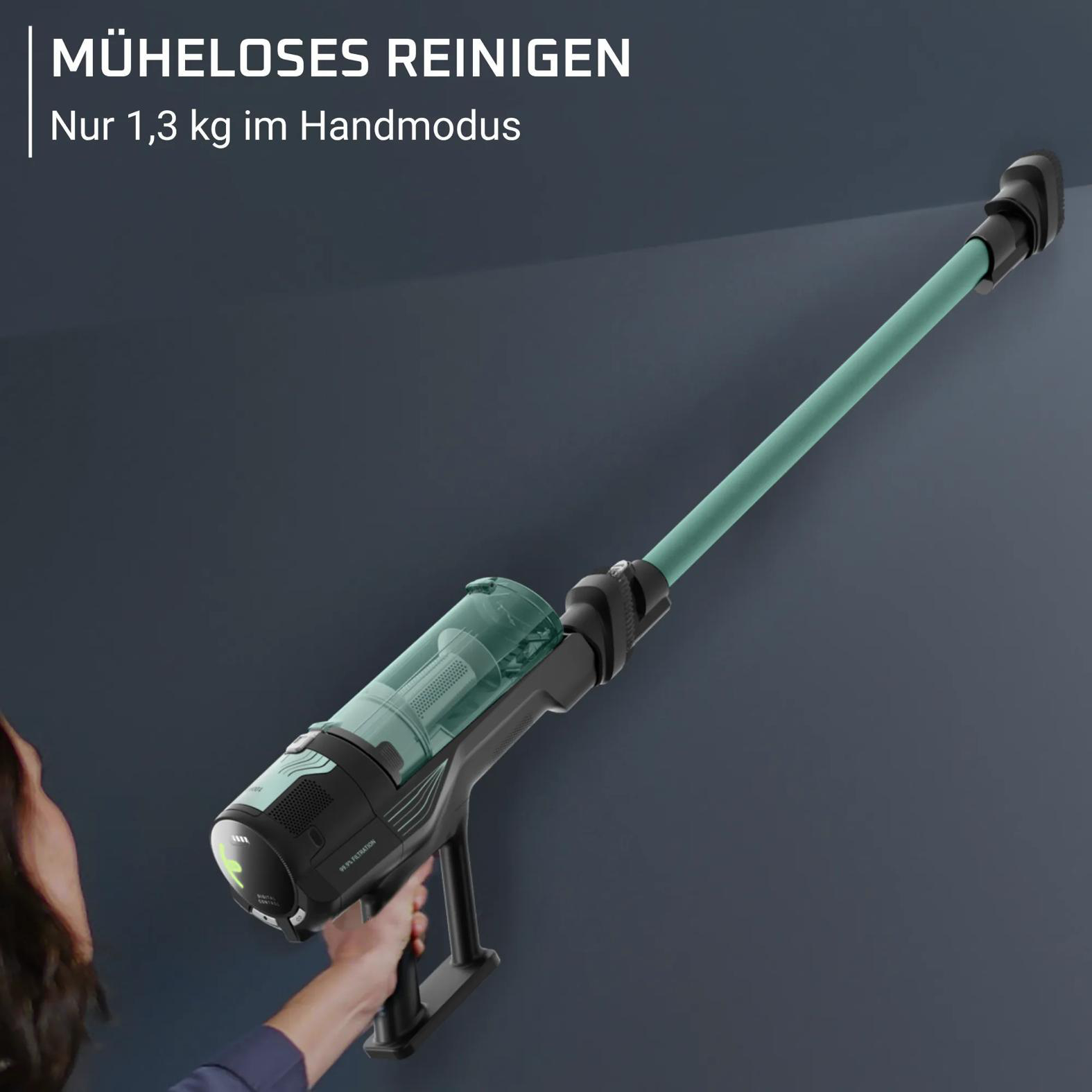 Handstaubsauger mit grünem Rohr wird von einer Hand gehalten, die ihn an einer Wand entlangführt.