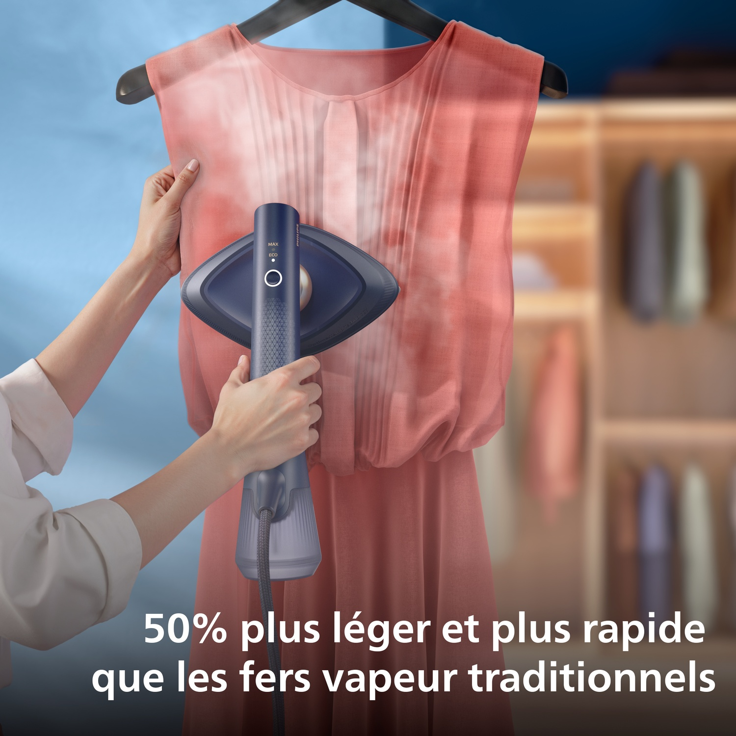 Une main tient un défroisseur pour lisser une robe corail. Une armoire est à l'arrière-plan.