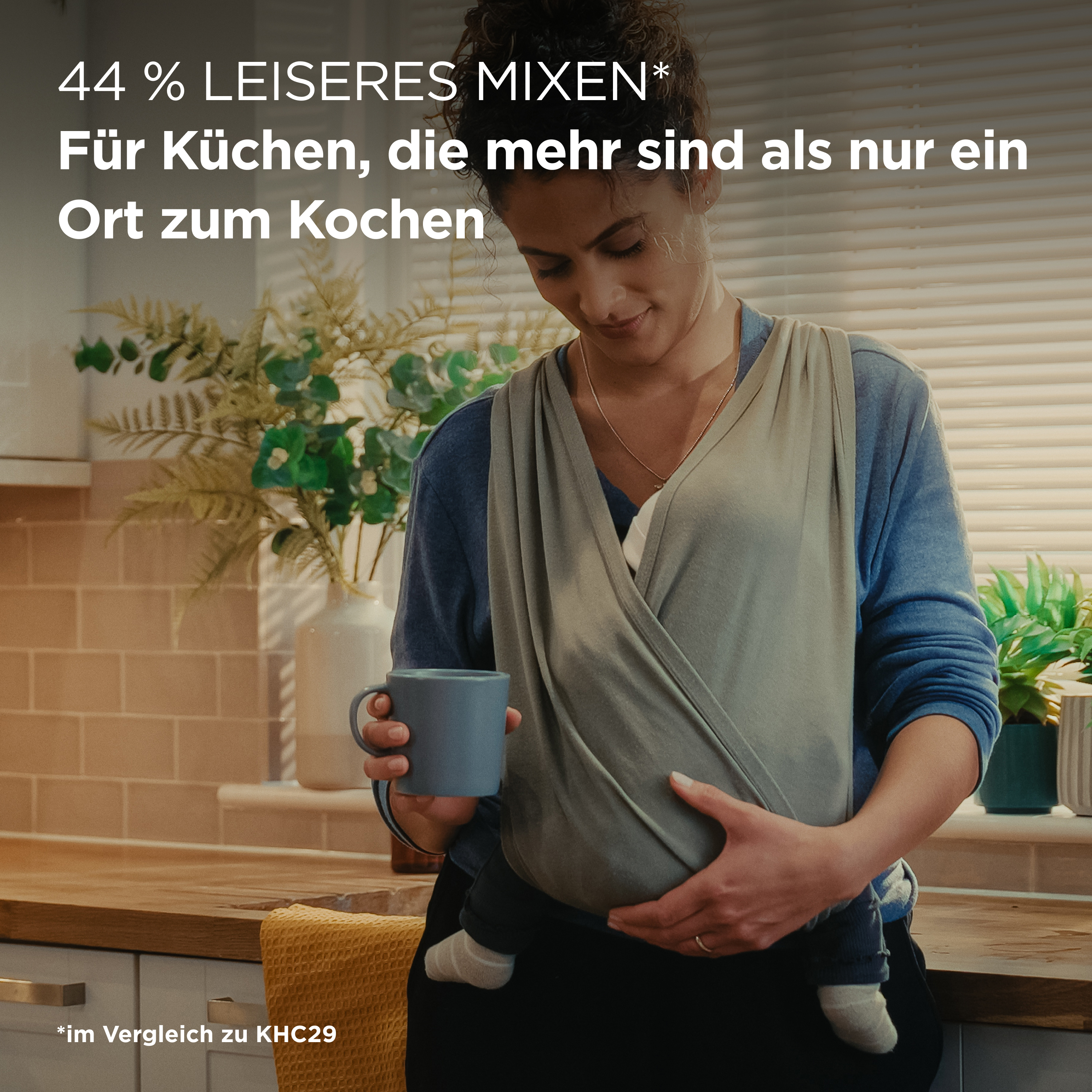 Eine Frau mit Babytrage in einer Küche hält eine Tasse, mit Text.