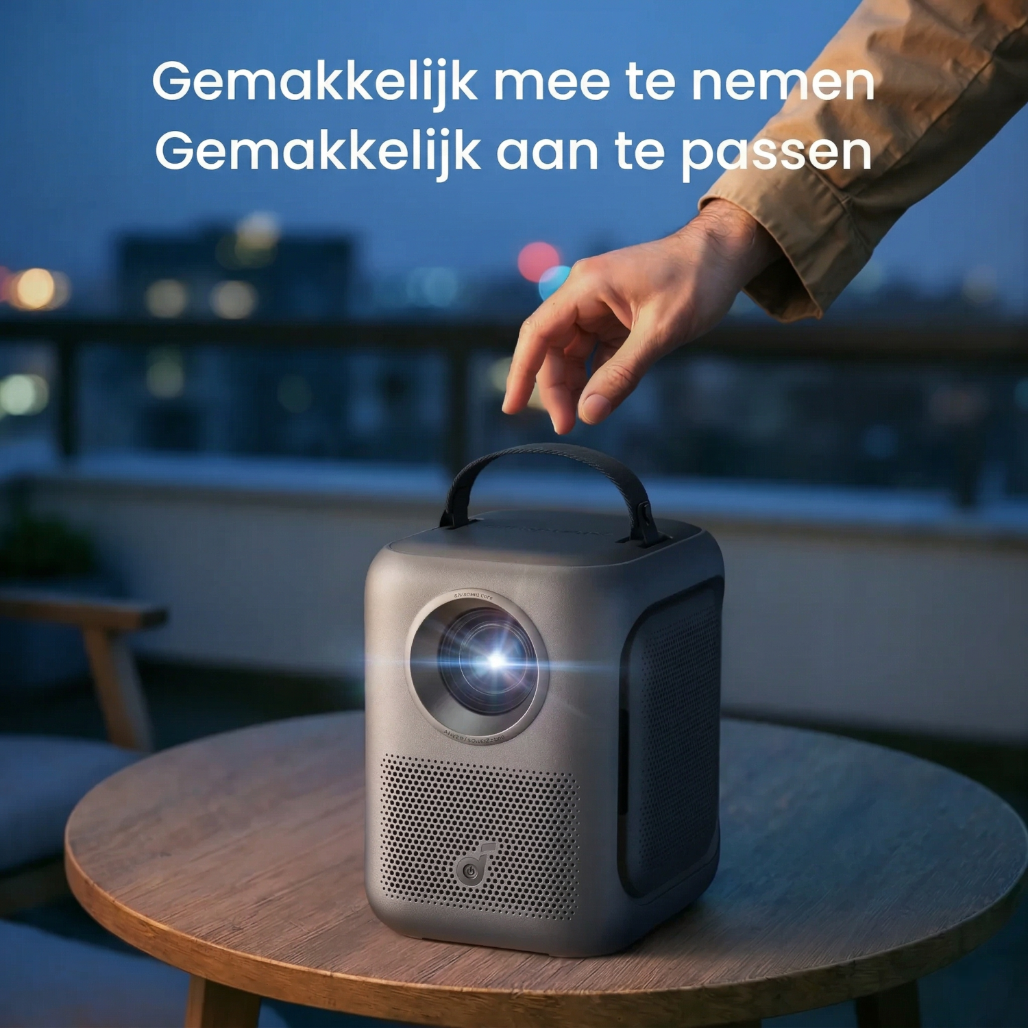 A portable projector on a wooden table, with a hand touching it.