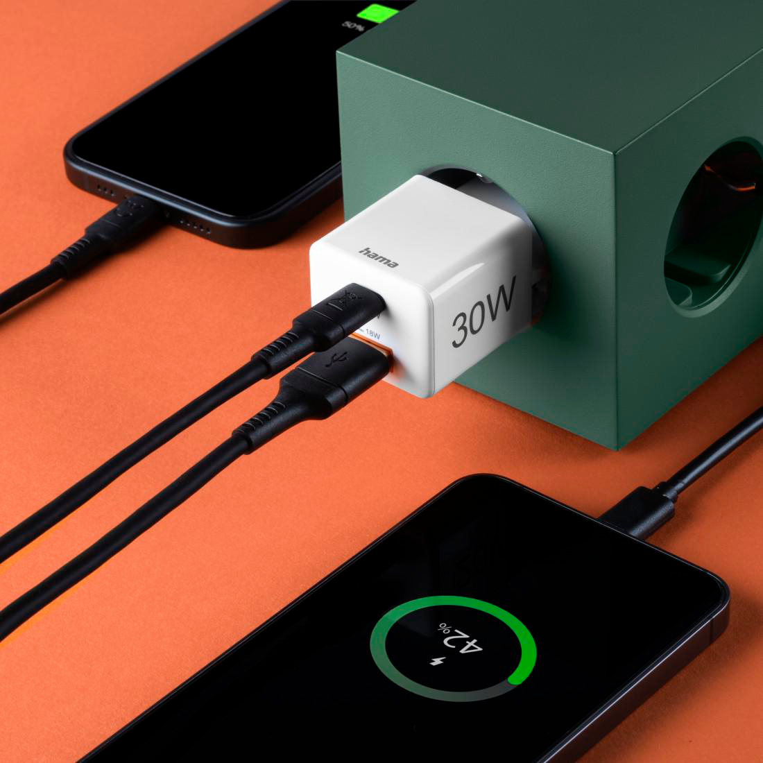 Ein weißer Hama 30W Ladeadapter steckt in einer grünen Ladestation. Zwei Kabel sind angeschlossen.