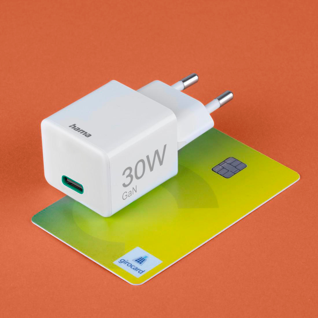 Ein weißer Hama 30W GaN Ladestecker liegt auf einer grünen Girocard.