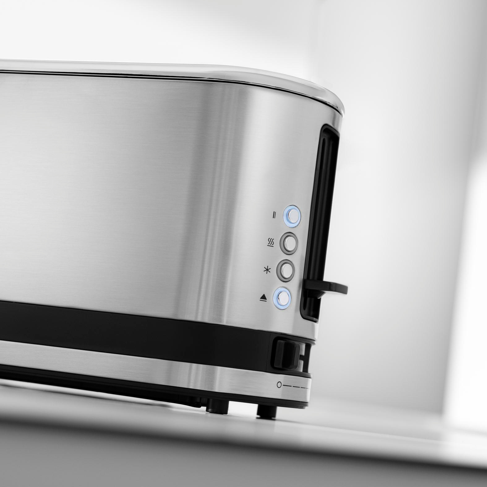 Silberner Toaster mit schwarzen Akzenten und beleuchteten Tasten auf heller grauer Fläche.