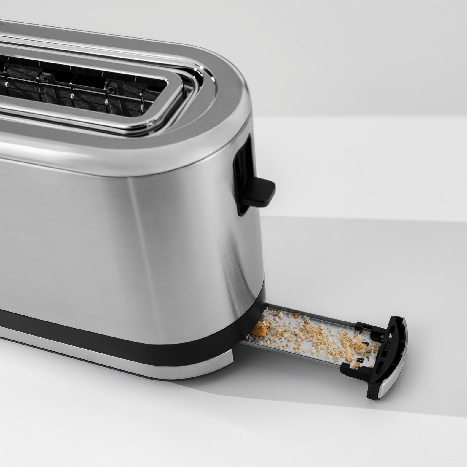 Silberner Toaster mit herausgezogener Krümelschublade, gefüllt mit Krümeln.